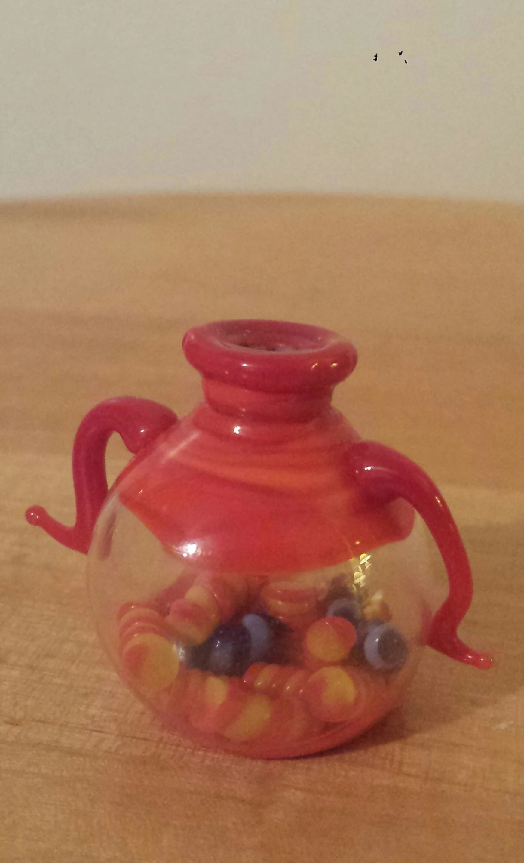 Colored glass pumpkin with orange, yellow, and purple circles, and red glass handles on a wooden surface.