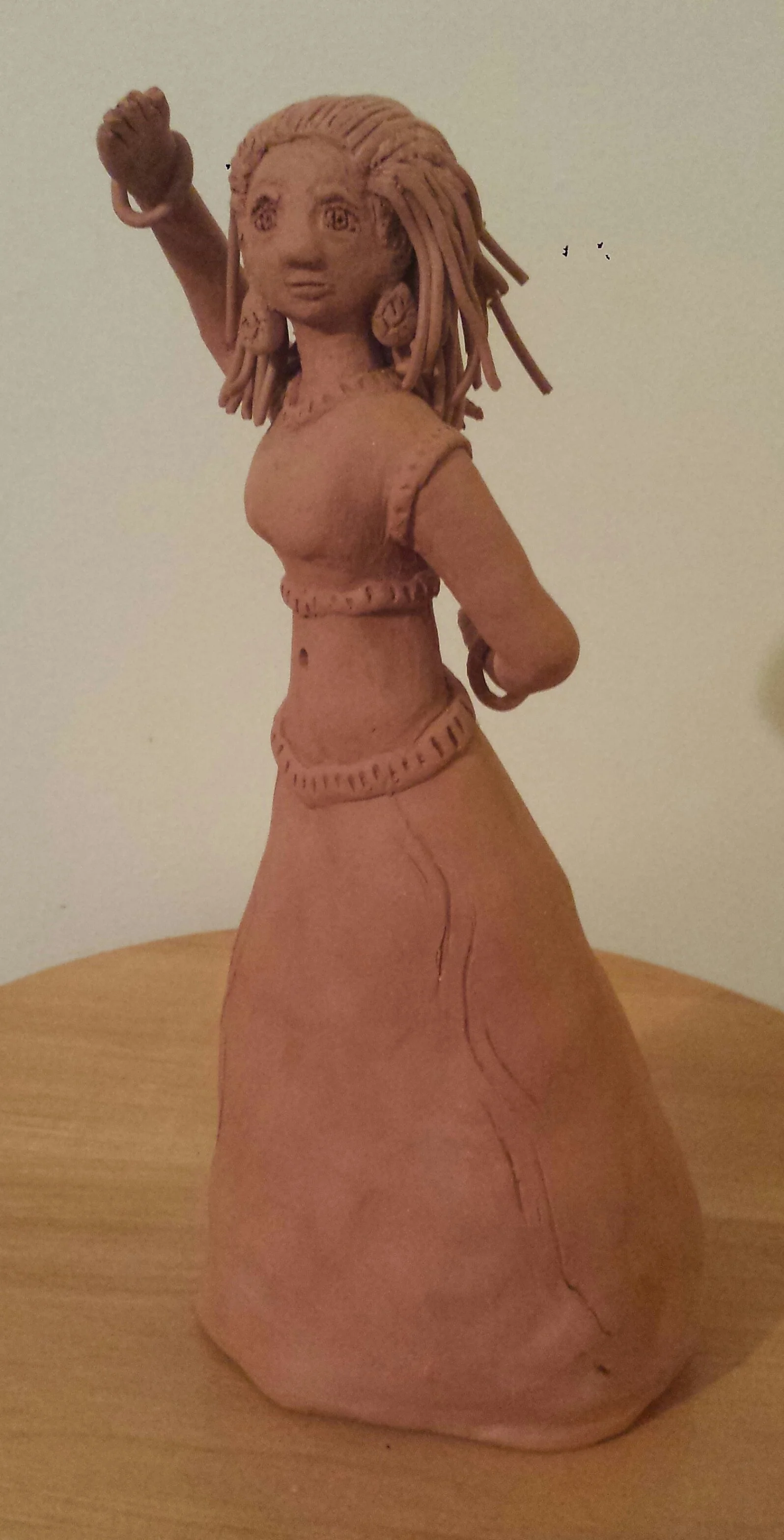 A sculpture of a woman with long hair, wearing a skirt and a crop top, with an arm raised in a fist.
