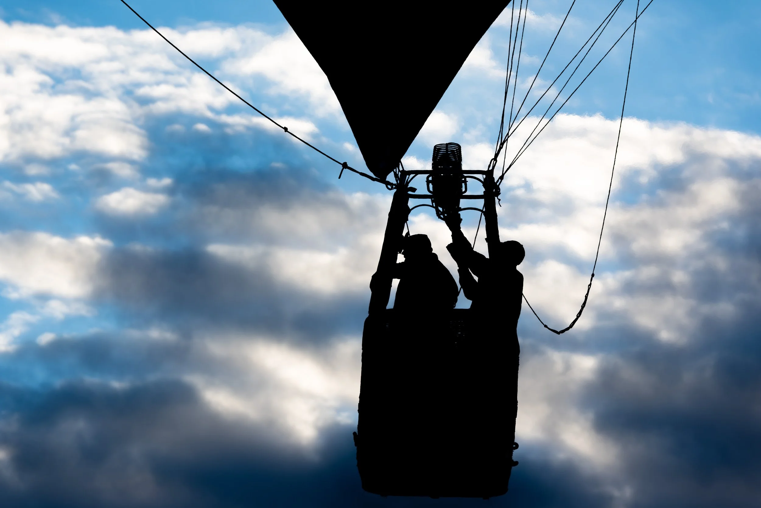 Silhouetted workers standing in a hot air balloon basket against a sky with clouds. © 2026 Outgear Adventure Photography. Bruce Maxwell - Albuquerque, NM
