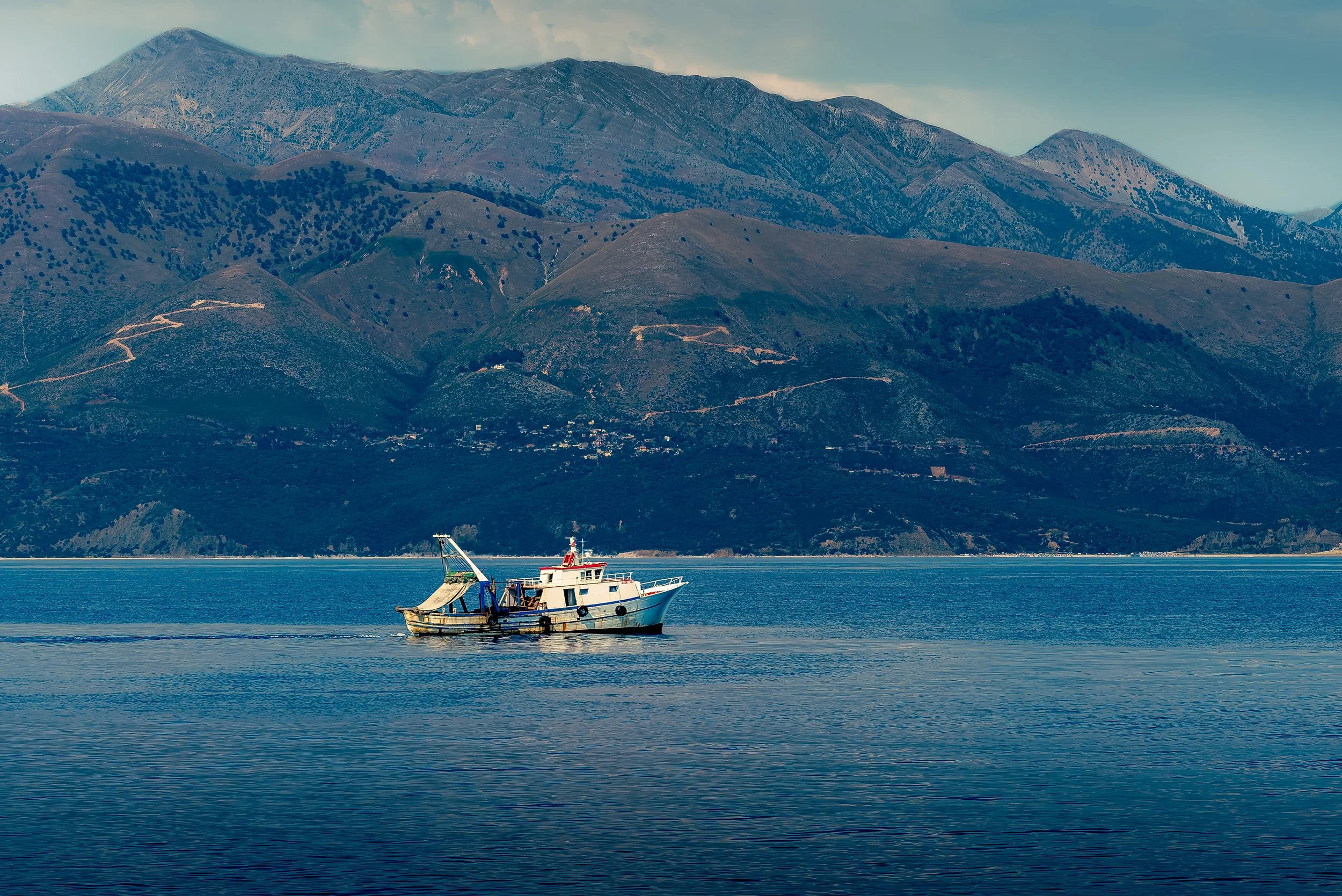 A boat floating on calm water with a mountain range in the background.