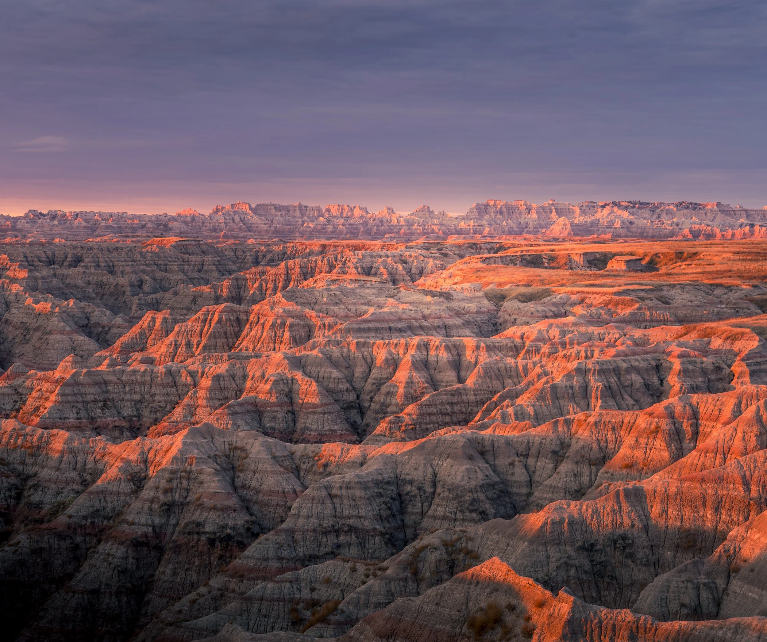 Sunset over colorful canyon landscape with layered rock formations and a partly cloudy sky.