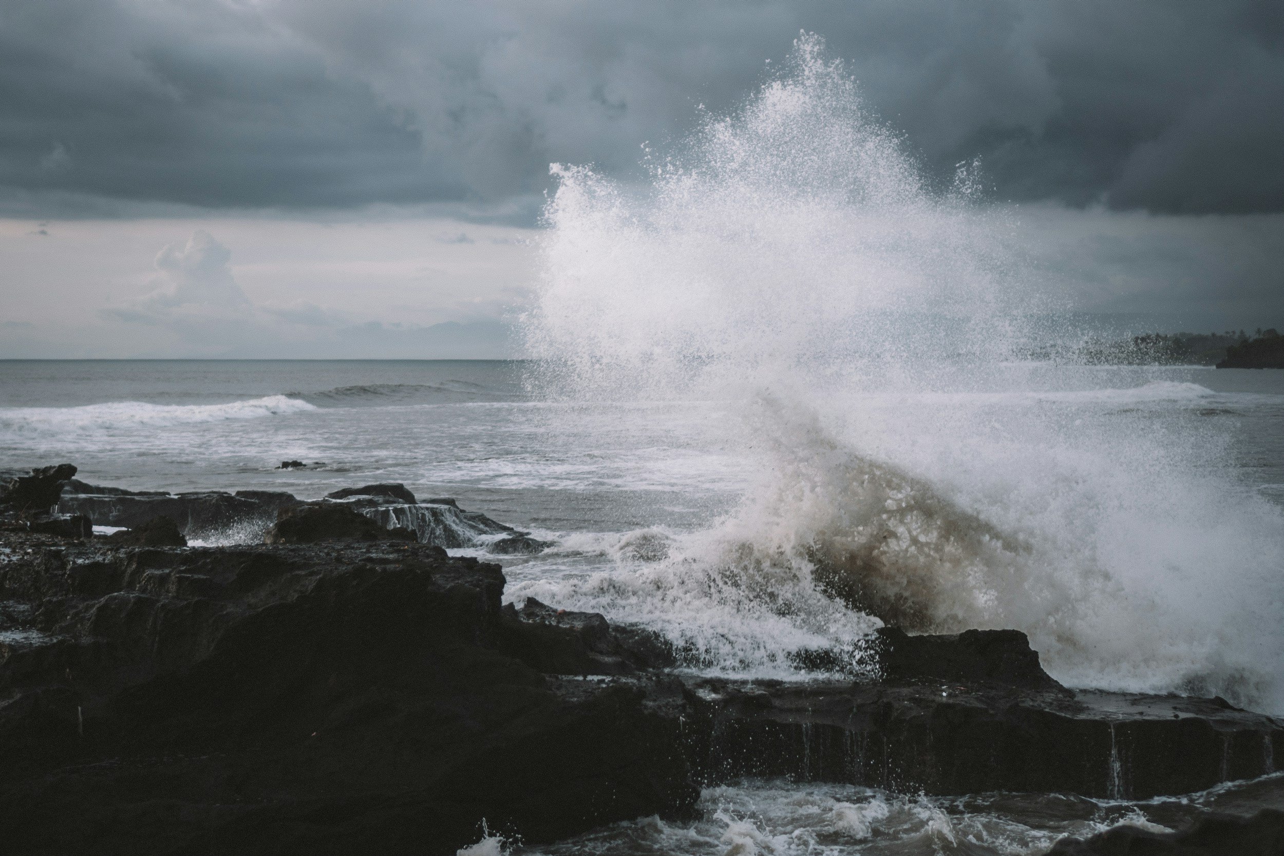Ocean waves crashing against rocky shoreline under dark cloudy sky.