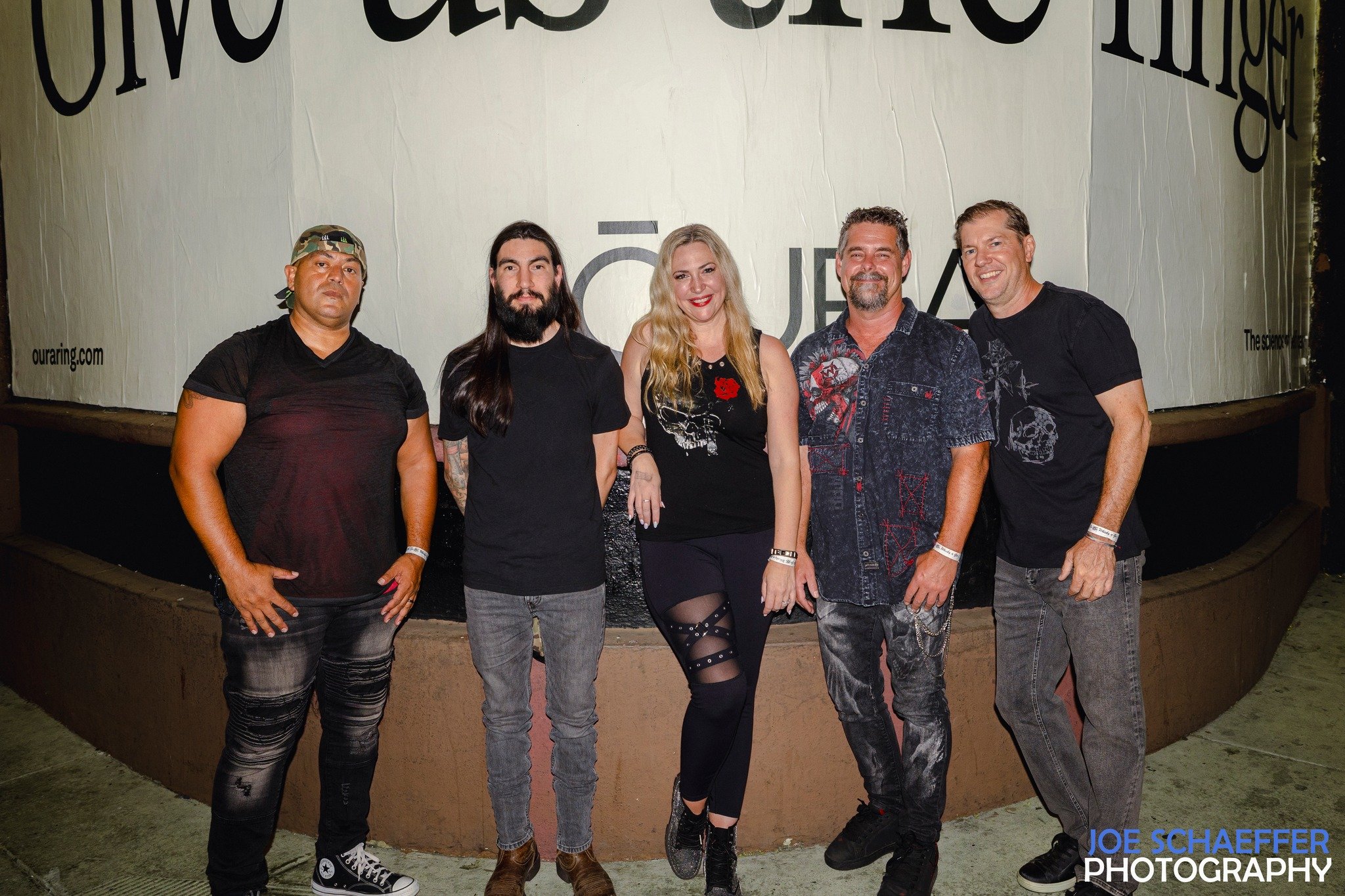 Group of five people standing together in front of a large sign with text, outdoors at night.