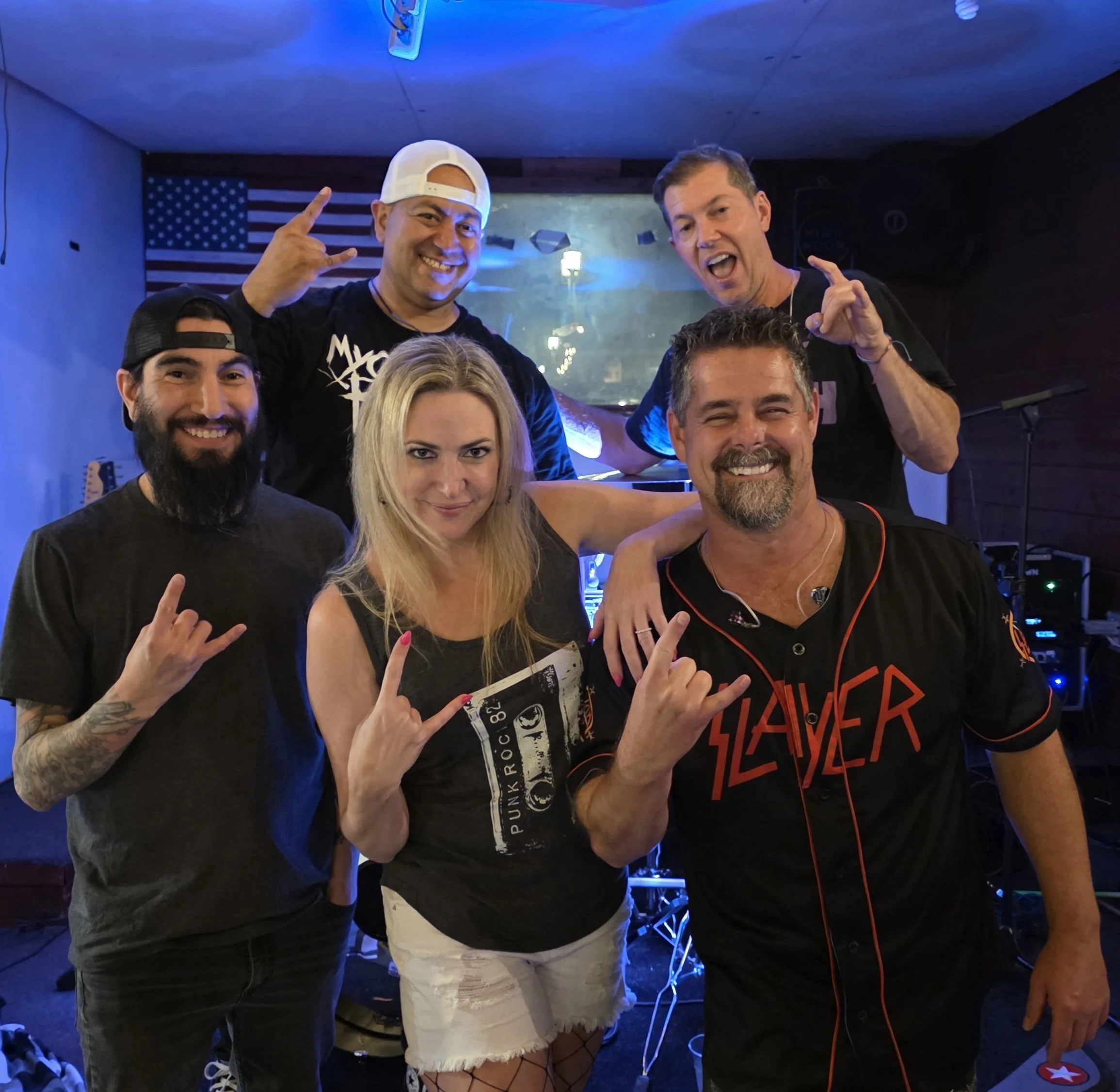 Group of friends smiling and making hand gestures in a bar or nightclub with American flag decoration and blue lighting.