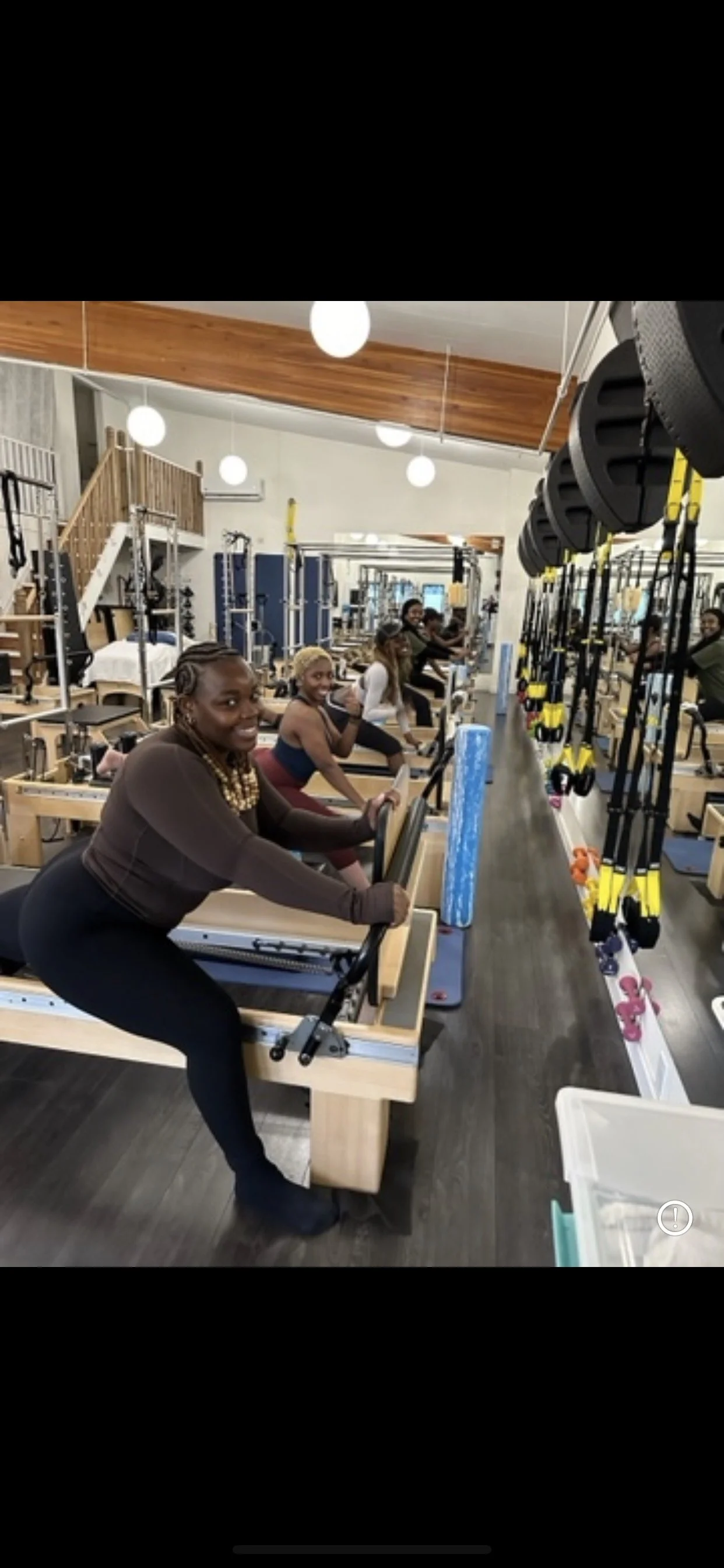 Women in a fitness studio using Pilates reformer machines, with exercise straps and foam rollers visible, and a mirrored wall in the background.