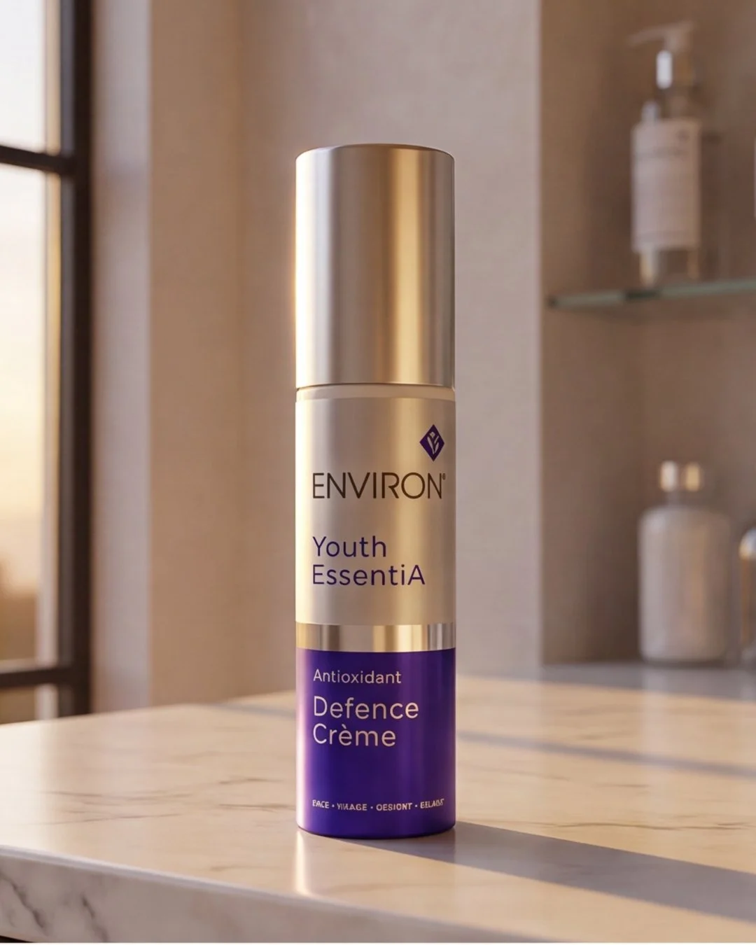 A skincare product bottle called Environ Youth EssentiA Antioxidant Defence Crème on a white marble surface inside a bathroom or spa, with blurred containers and shelving in the background.