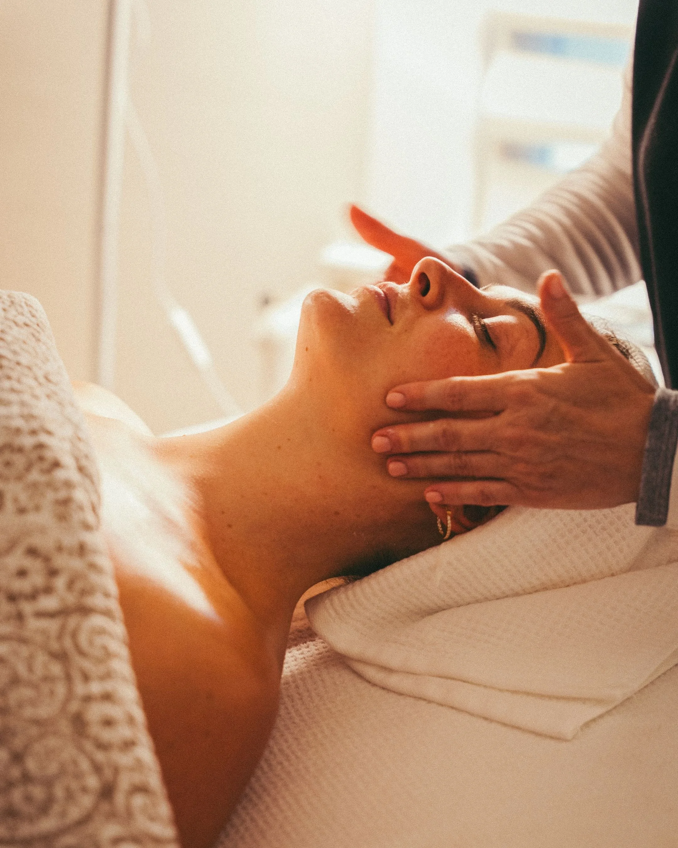 A woman receiving a facial massage from a massage therapist in a spa setting with warm lighting.