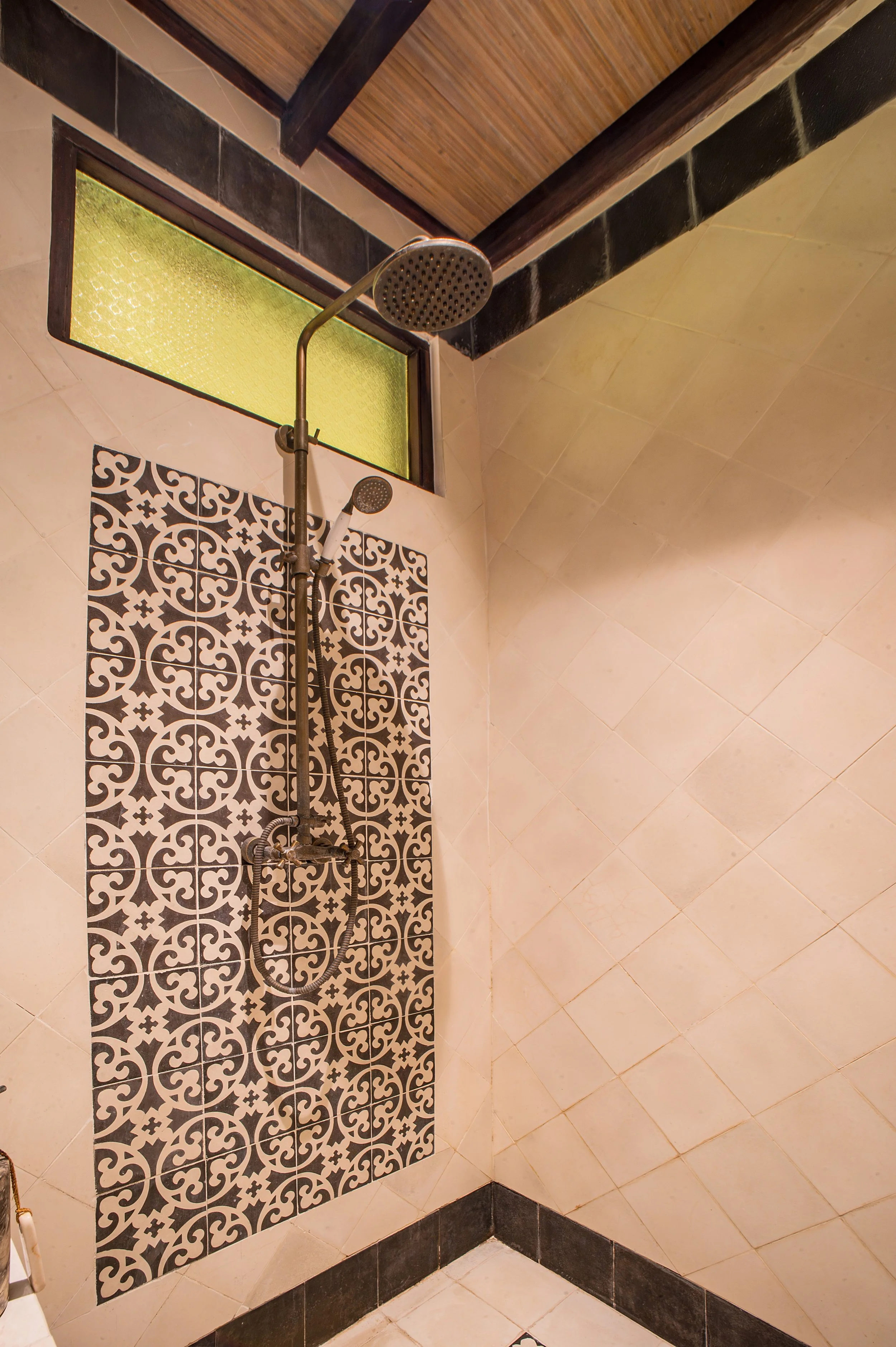 A shower area with a decorative black and white patterned tile wall, a handheld showerhead, and a window with frosted yellow glass.