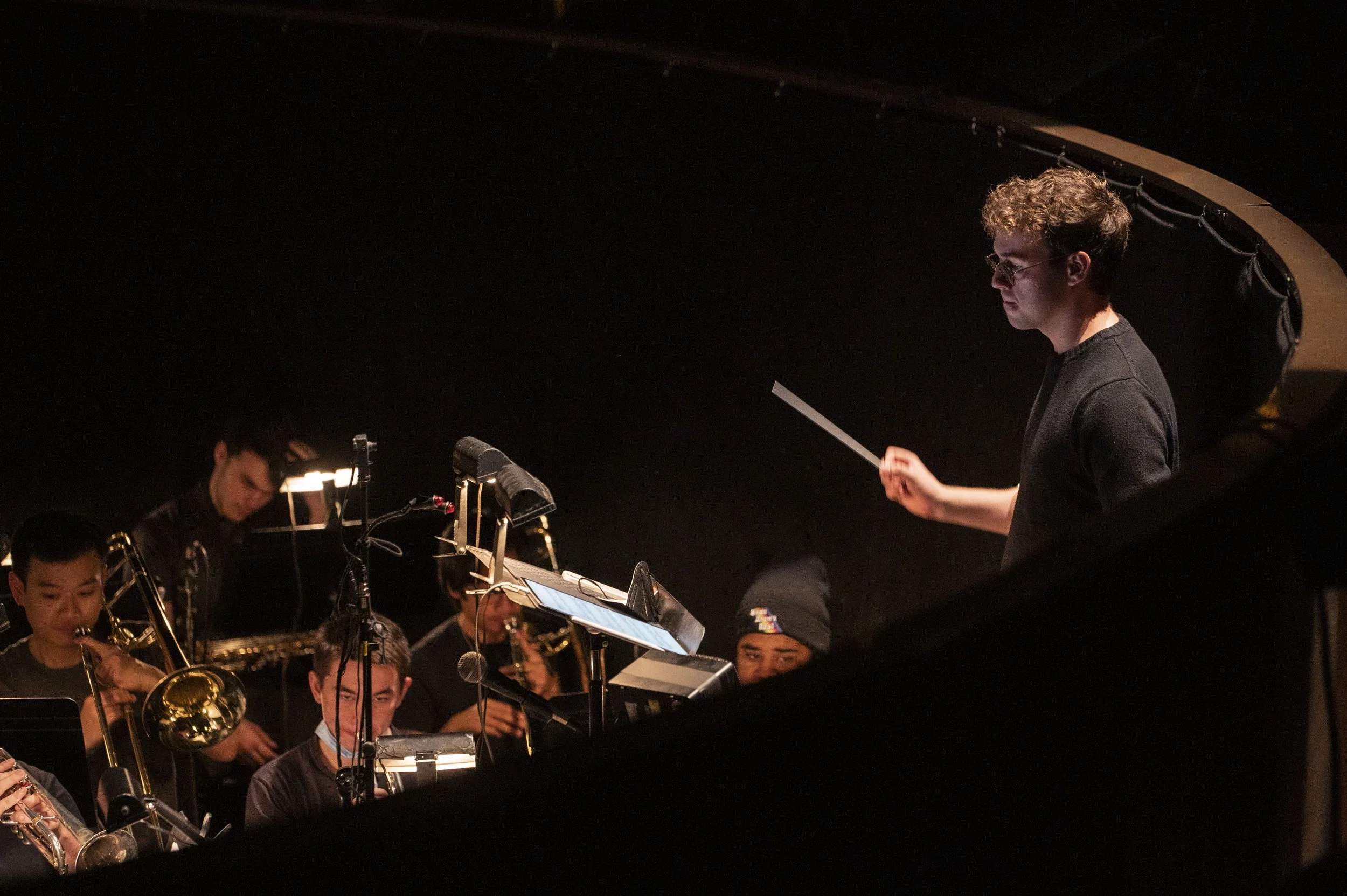 Andrew leading an orchestra during a performance, with musicians playing various instruments in a darkened theater.
