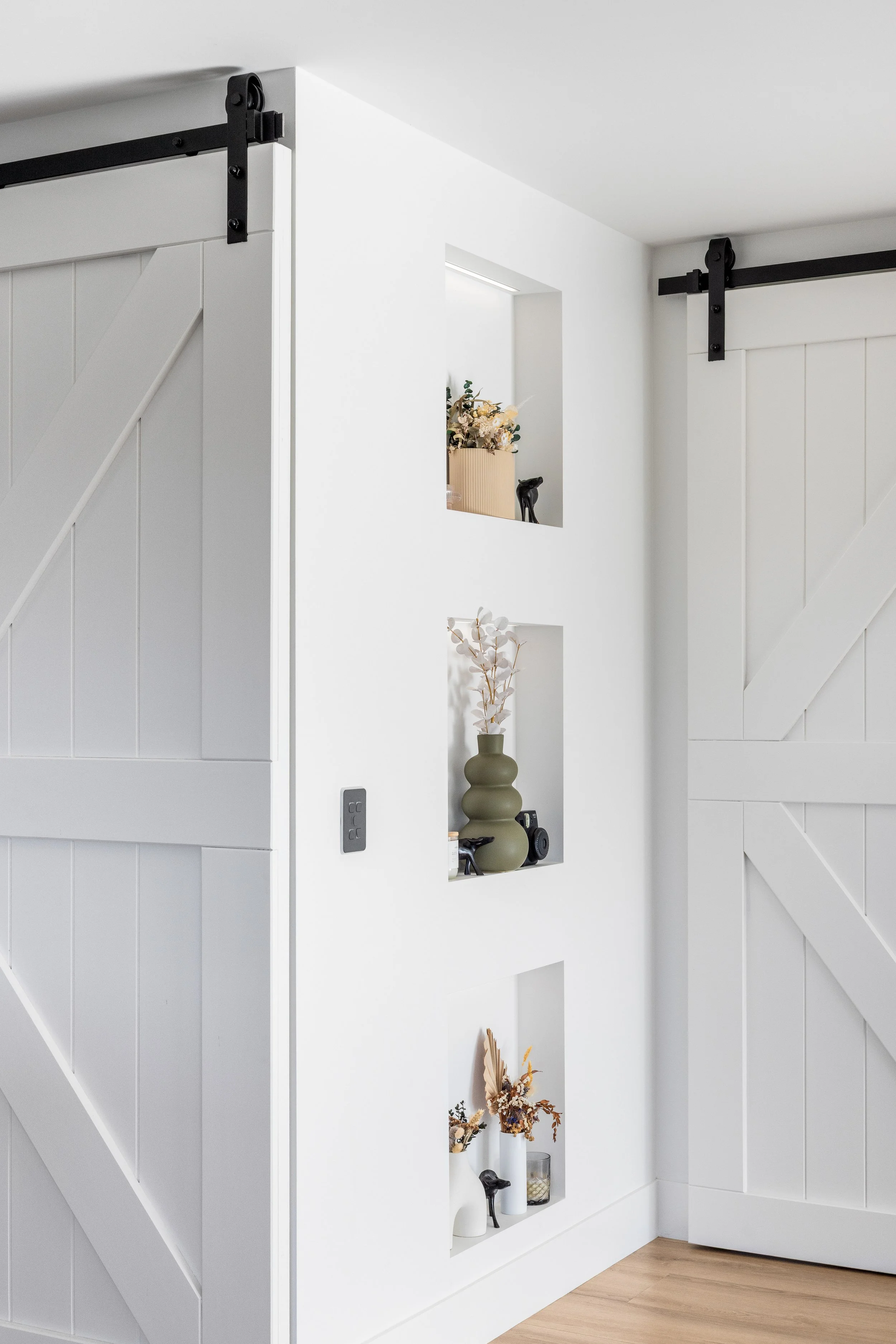 Interior of a modern house with built-in white shelves displaying decorative items, with barn door hardware visible on the side.