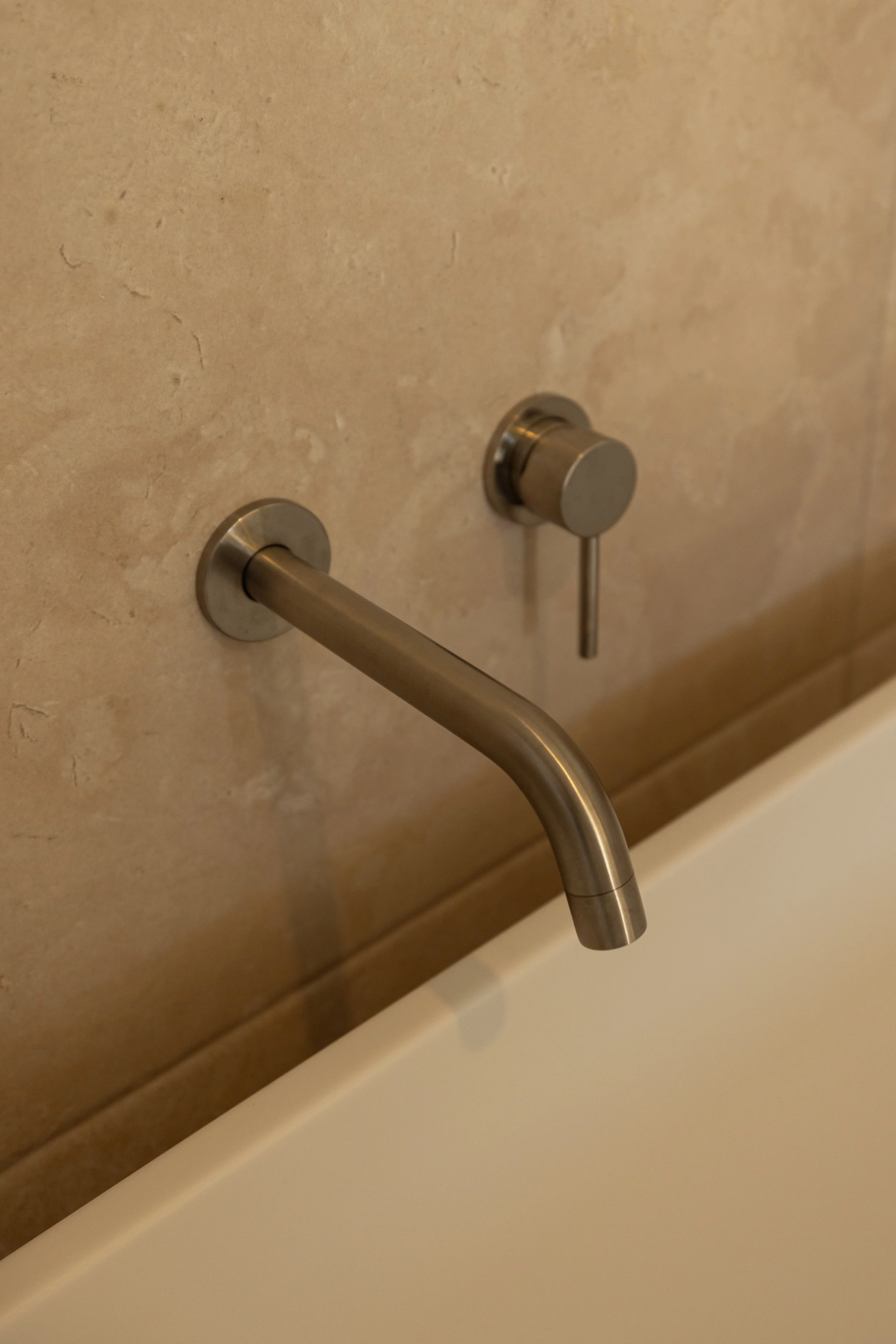 Close-up of a stainless steel faucet against a beige tiled wall.