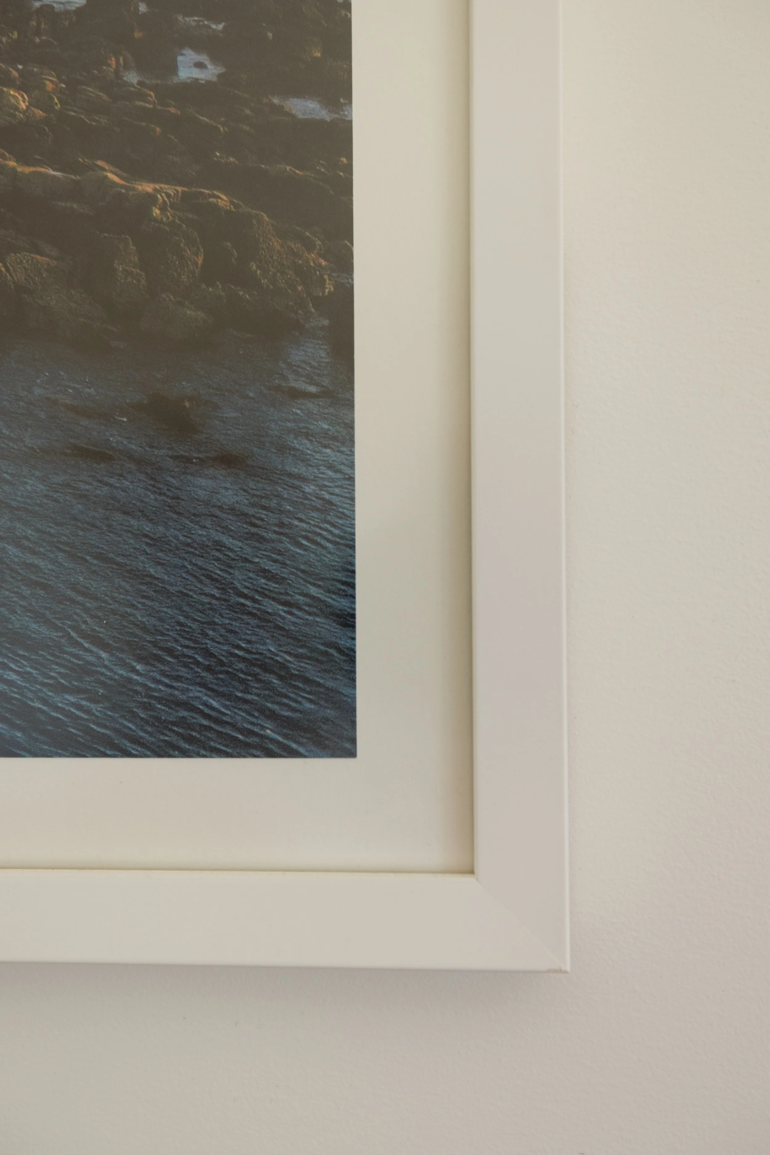 Close-up of a framed photograph showing a rocky shoreline with water, mounted on a wall.