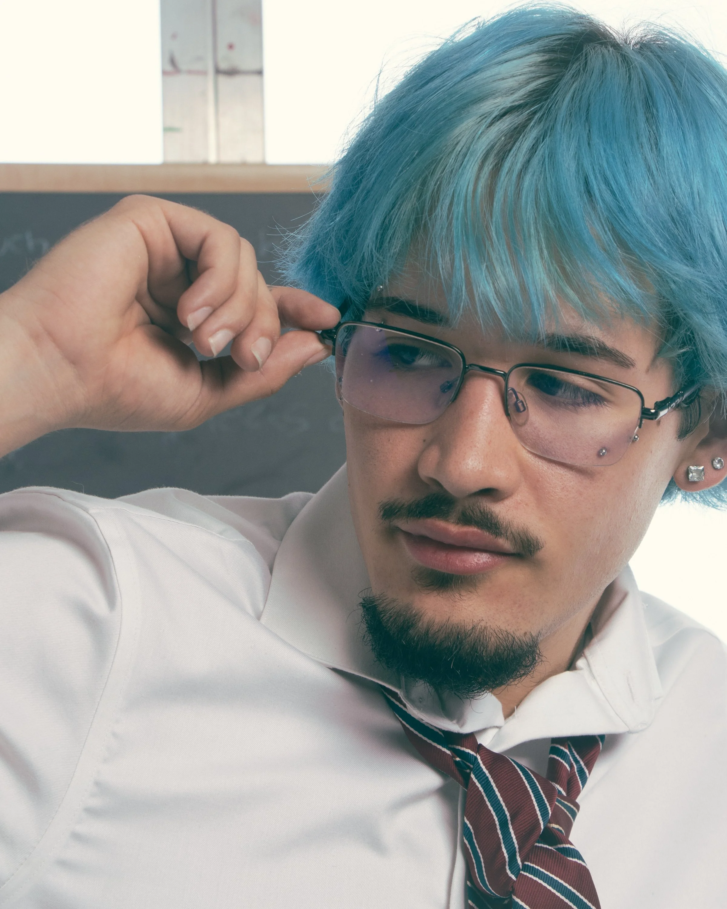 A person with blue hair and glasses adjusting their glasses.