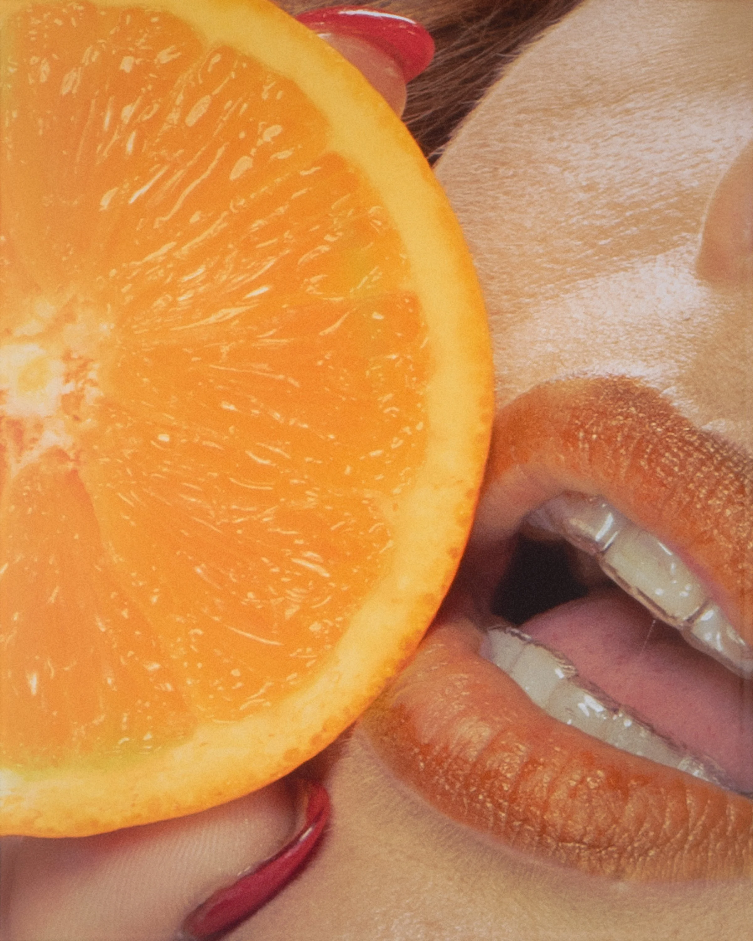 Close-up image of a sliced orange, caramelized chocolate, and a glass of red wine. The orange half is in the foreground, showing its juicy interior. The chocolate appears to be covered in caramel or sugar, and the wine glass is partially visible with