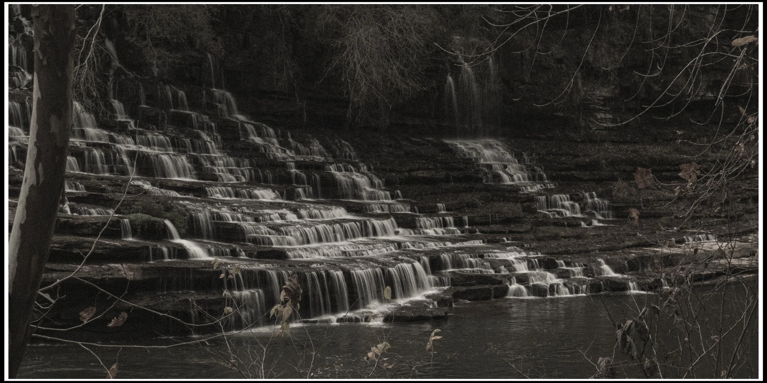 Nighttime scene of a multi-tiered waterfall with water flowing over rocks, surrounded by leafless trees.