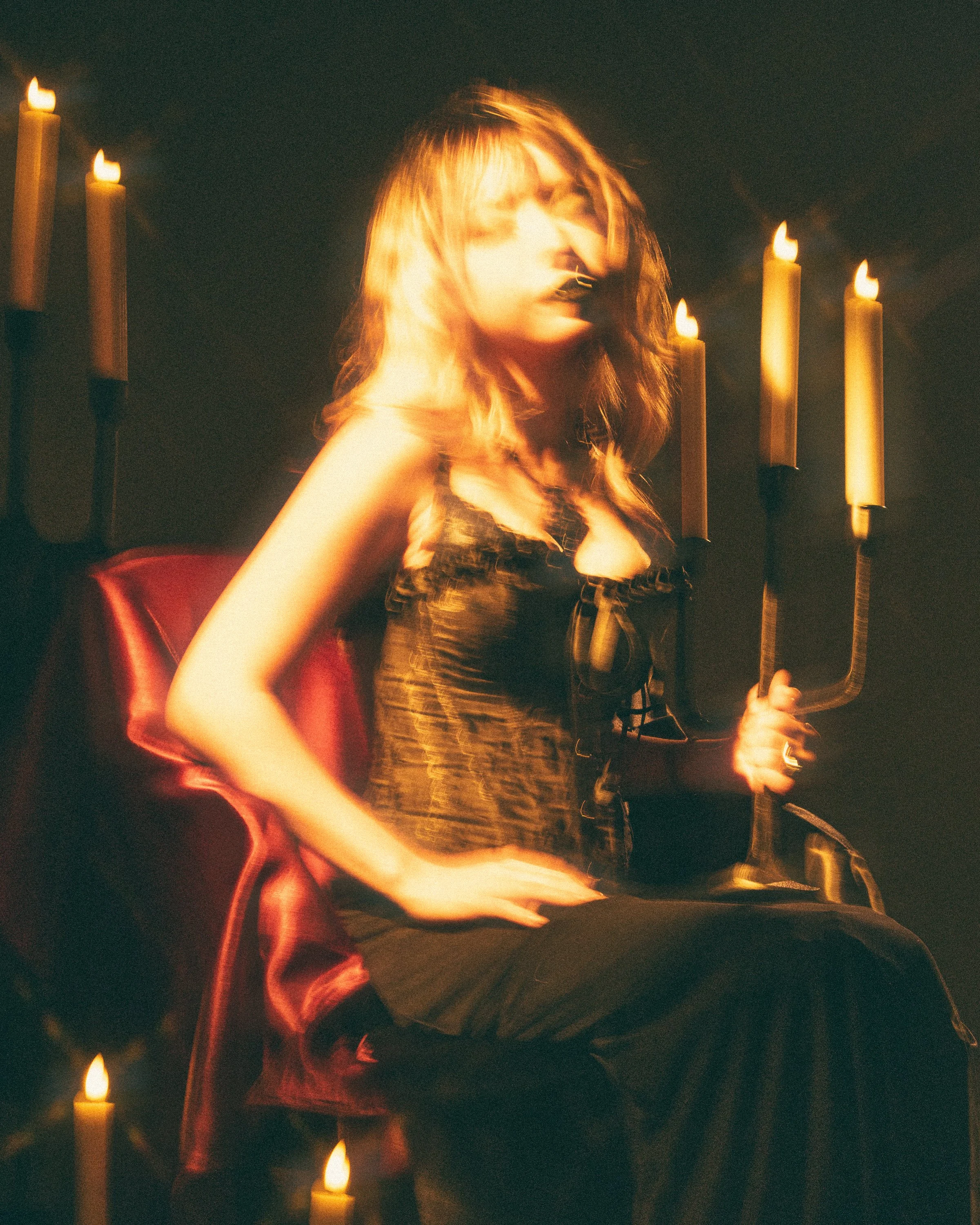 A woman with shoulder-length blonde hair sitting in a dimly lit room decorated with candle sconces, holding a large U-shaped pipe suspirator, with a slightly blurred expression.
