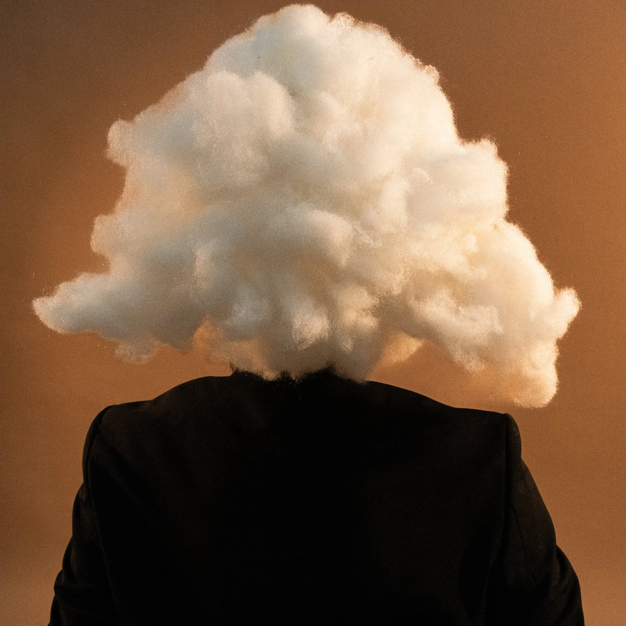 A person wearing a hoodie standing outdoors at dusk, with a large, fluffy cloud in the sky illuminated by streetlights.