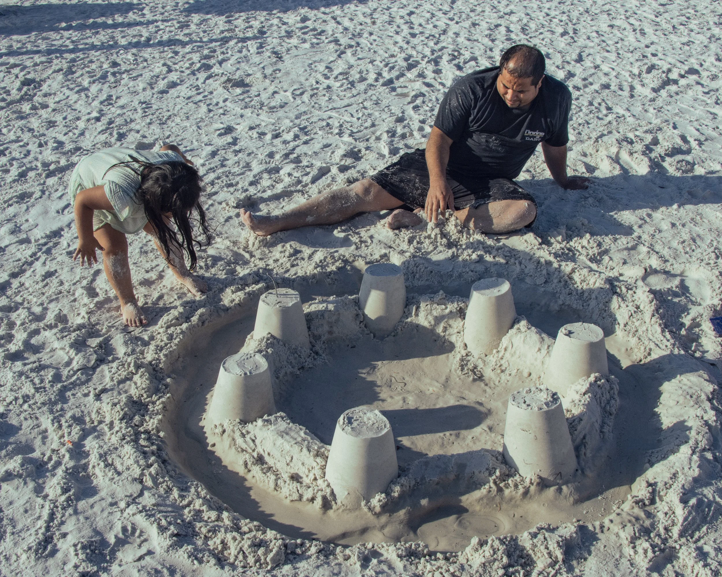 Children and an adult building sandcastles on a snowy beach.