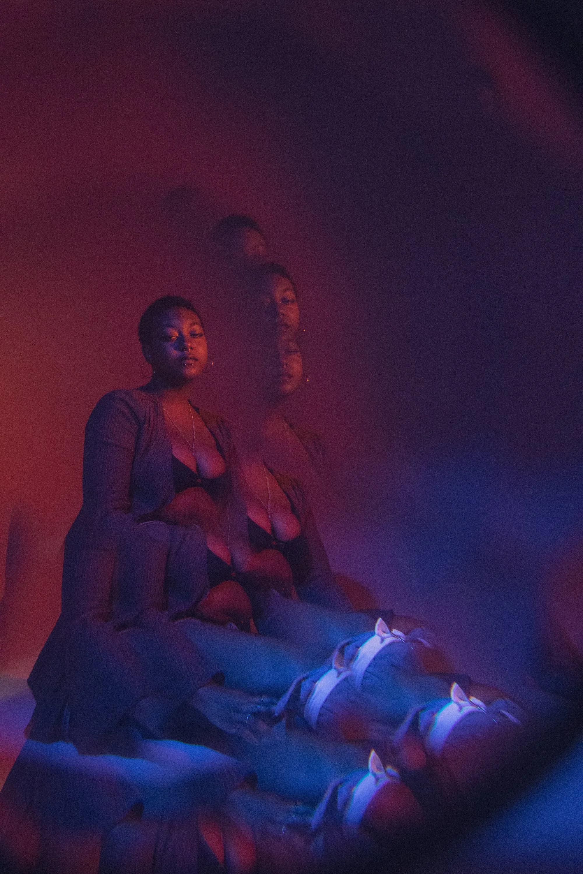 Three women sitting against a gradient colored background with pink, purple, and blue hues, with their reflections creating layered images.