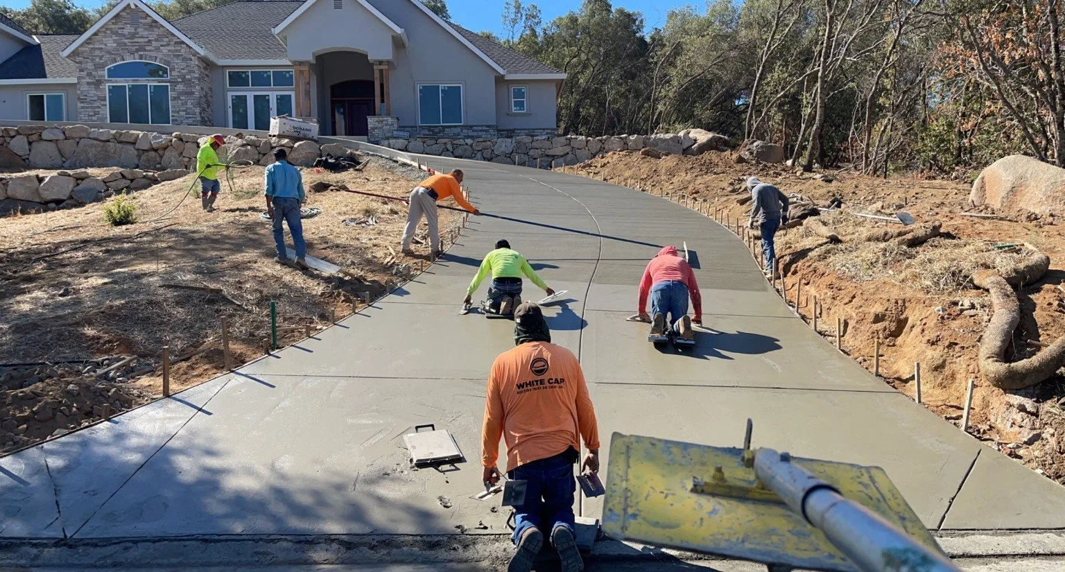 Construction workers pouring and smoothing concrete on a driveway in front of a house.