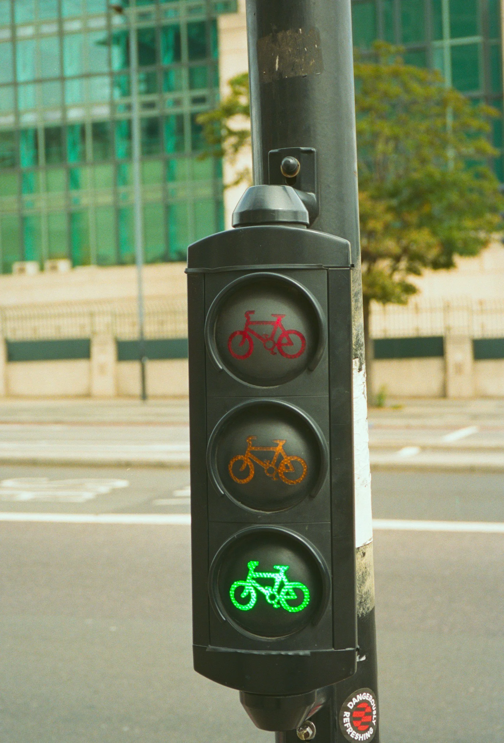 A traffic light with green, yellow, and red bicycle signals, mounted on a pole at an intersection.