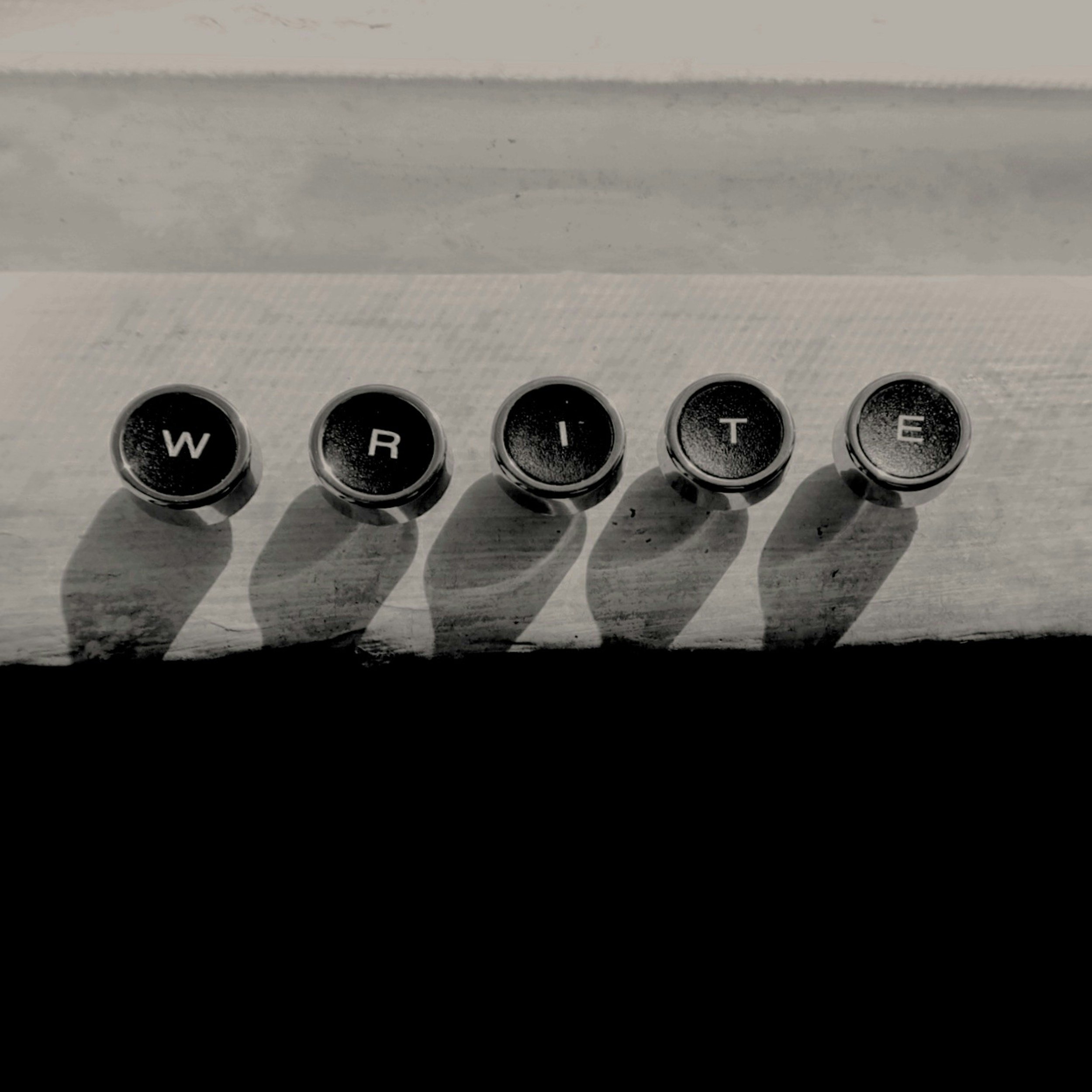 Close-up of a typewriter with typed keys W, R, I, T, and E visible, with shadows cast on the keys.