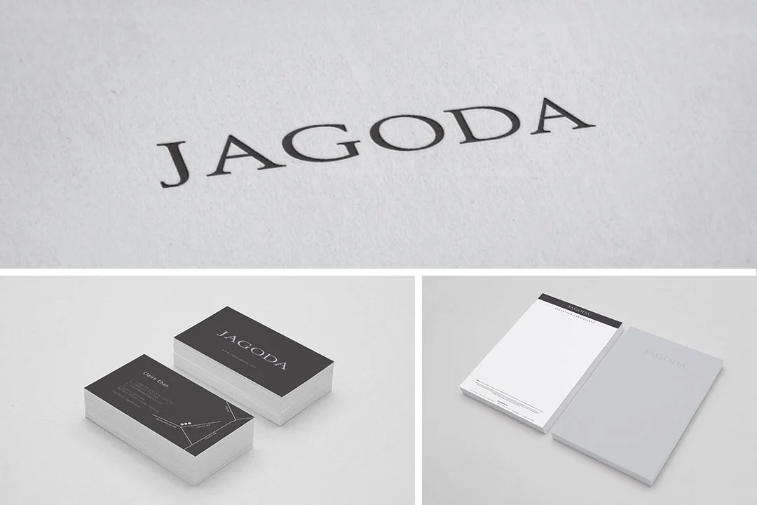 Close-up of the word "JAGODA" printed in black capital letters on white paper, with business cards and notepads featuring the same branding in a minimalist design.