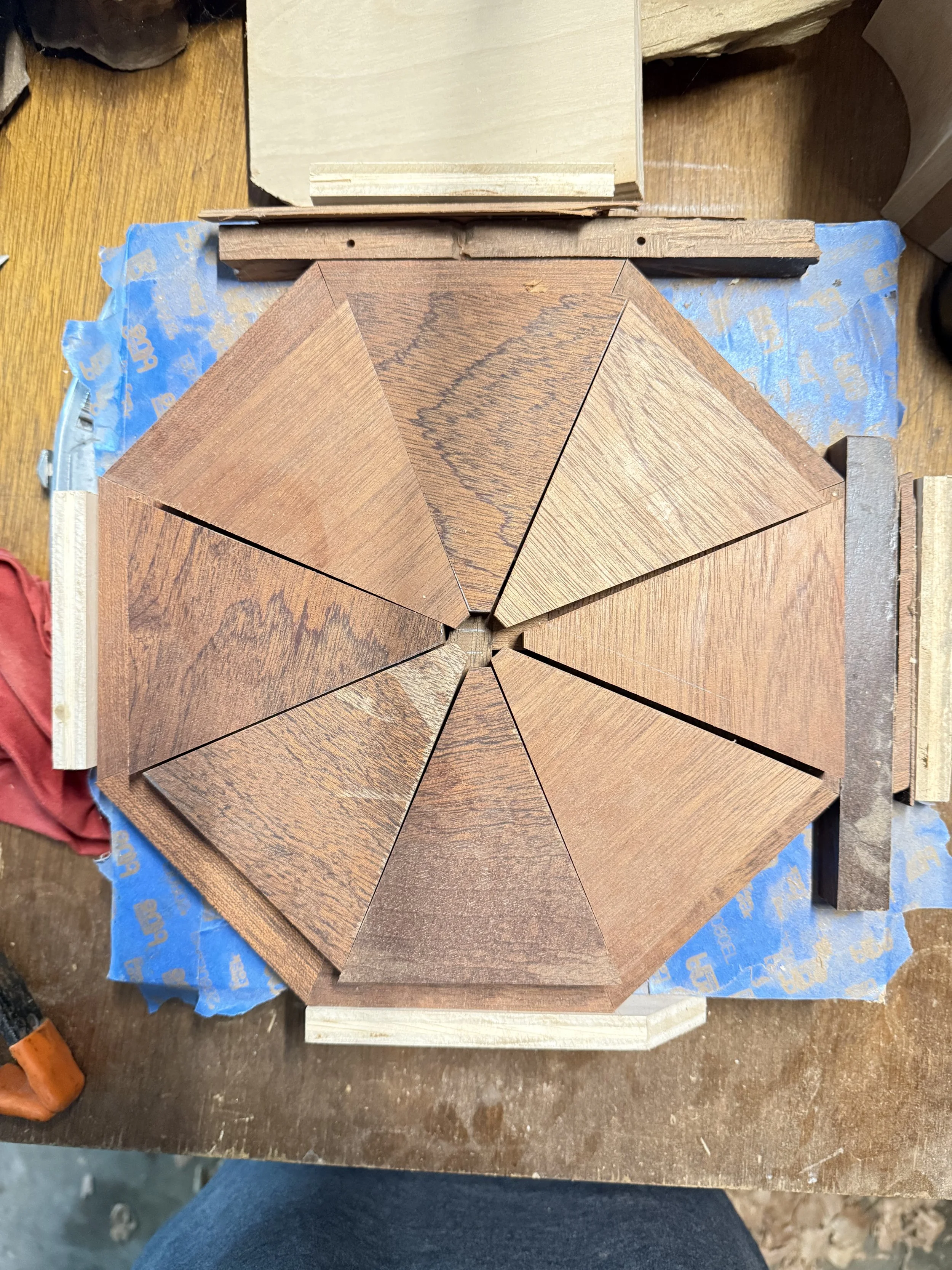 Top-down workbench view of eight individual dark wood triangles arranged in an octagon shape being aligned in a custom studio template jig for a geometric modern sculpture by BeckerDzine in Kansas City.