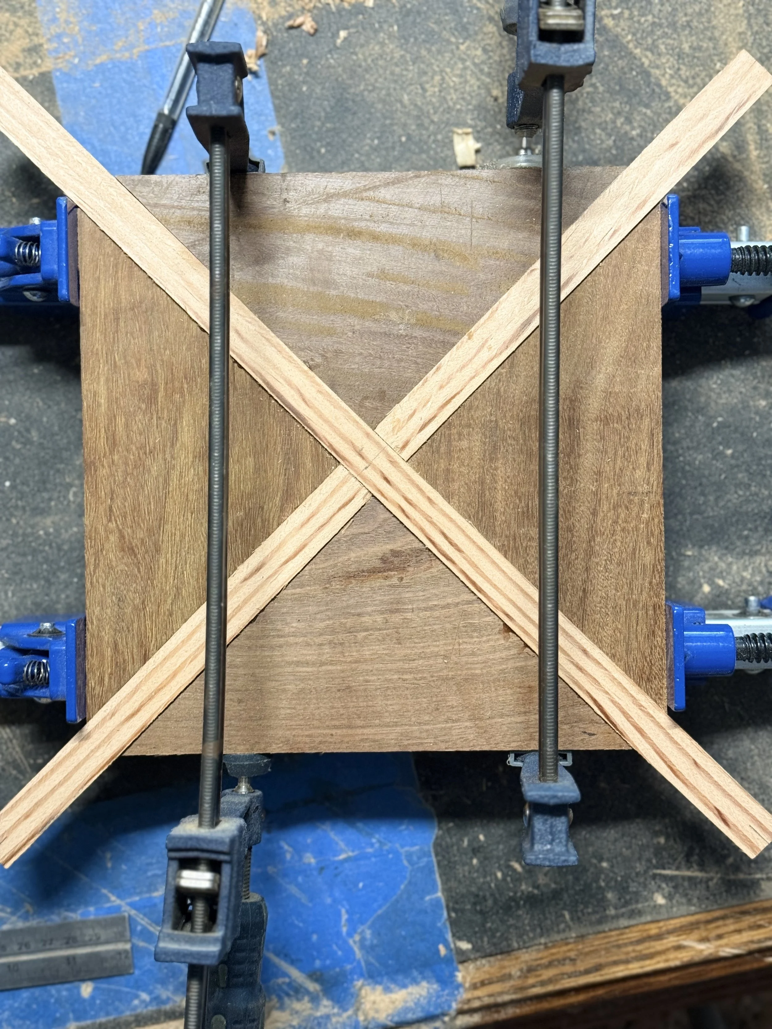 Top-down workbench view of geometric wood inlay channels being glued and clamped into a dark timber base block for a modern sculpture by BeckerDzine in Kansas City.