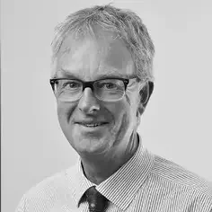 Black and white portrait of a man with short gray hair, glasses, and a collared shirt with a tie.