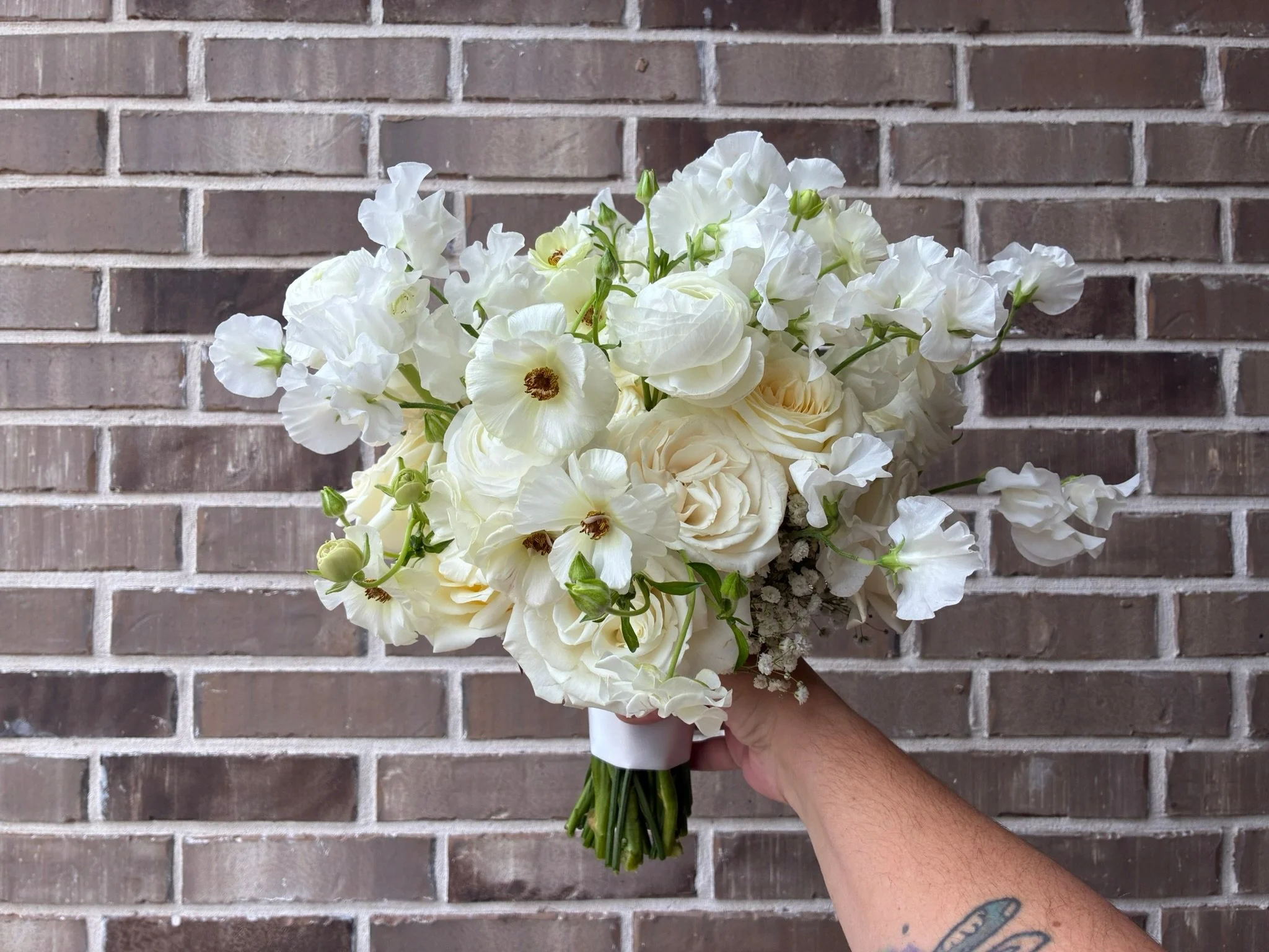 A hand holding a bouquet of white flowers with a brick wall background.