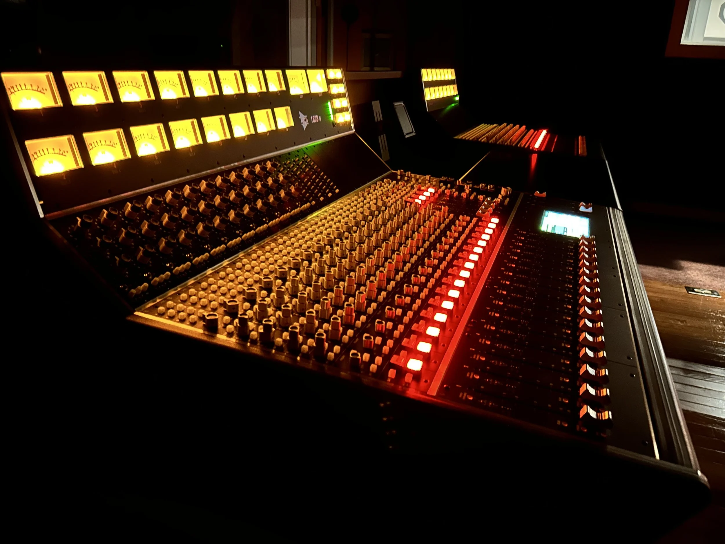 A music mixing console with multiple illuminated dials and sliders in a dimly lit room.