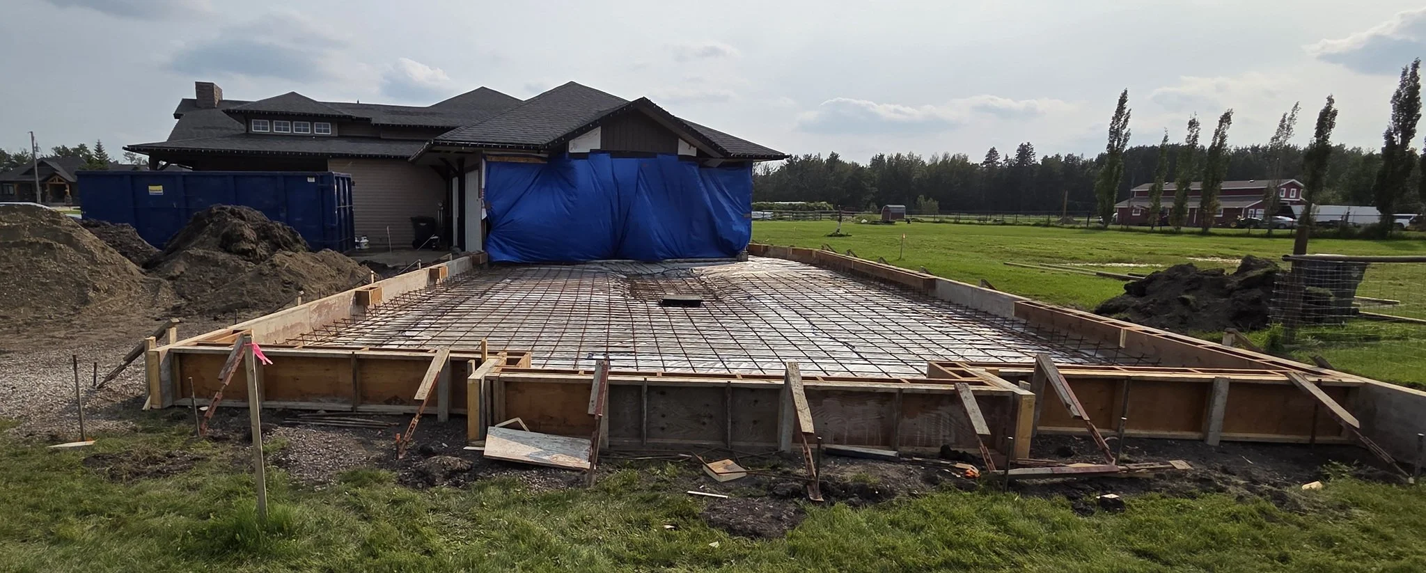 A large-scale custom residential concrete driveway base preparation featuring structural wood formwork and tightly bound steel rebar grid on a luxury Alberta acreage estate.