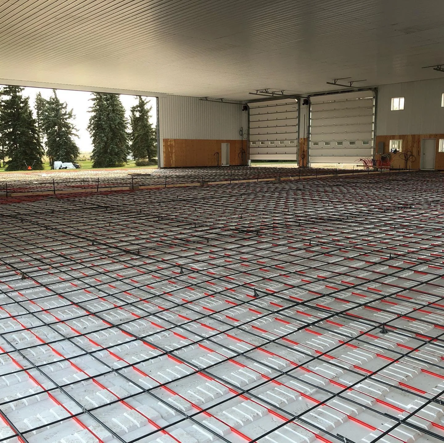 An expansive industrial shop floor under construction featuring a massive radiant heating PEX pipe grid and steel mesh reinforcement before a commercial concrete pour in Leduc