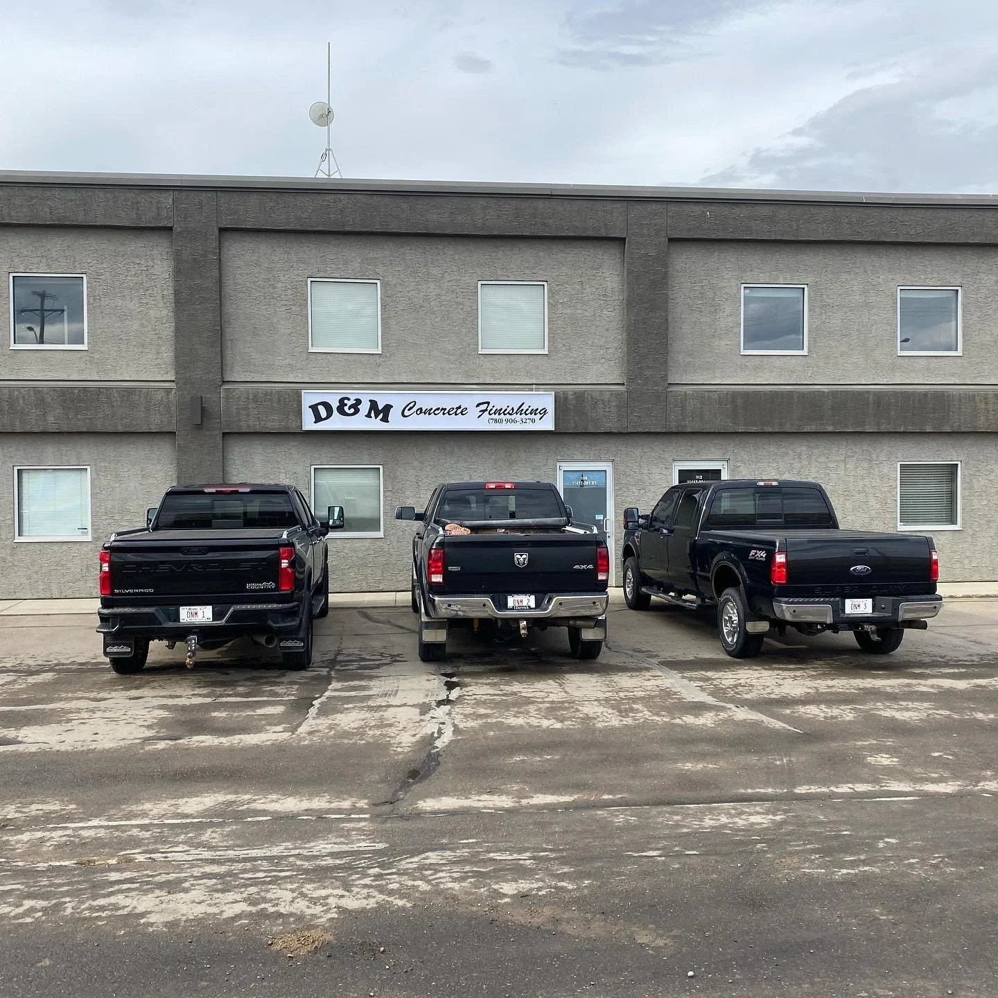 The DM Concrete commercial headquarters and fleet mobilization yard featuring professional trade trucks parked outside the main office building in Acheson.