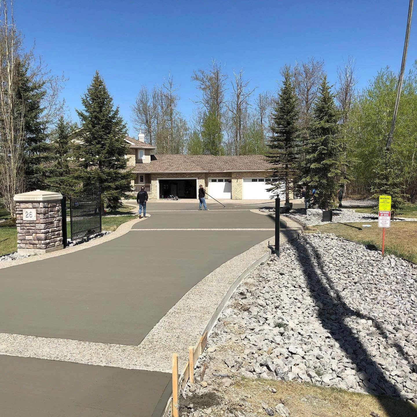 Workers smoothing fresh asphalt in driveway of a house, with trees and a blue sky in the background.