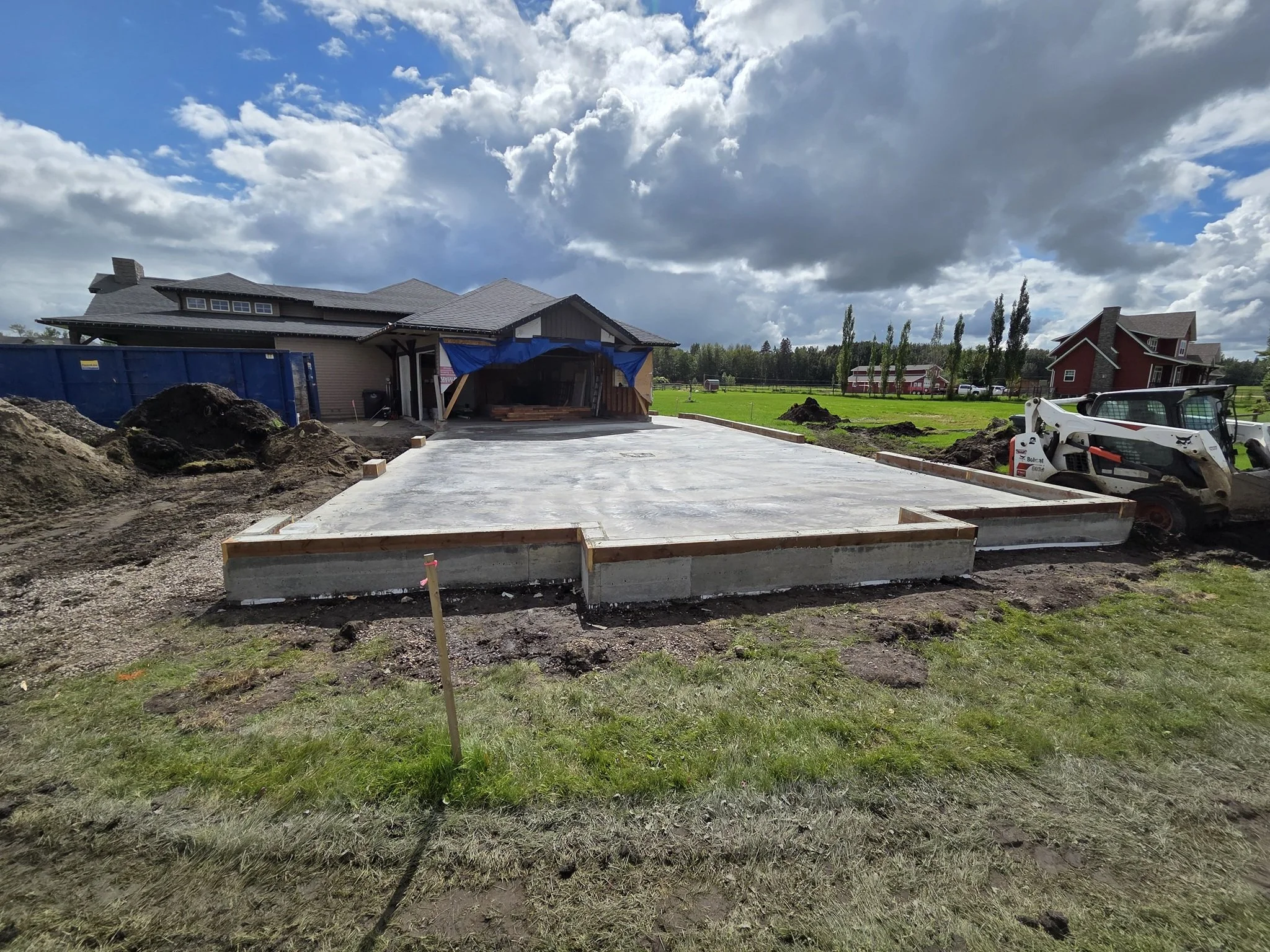 A completed large-scale structural concrete driveway pad with stripped forms and heavy equipment on a luxury Parkland County acreage estate near Spruce Grove.