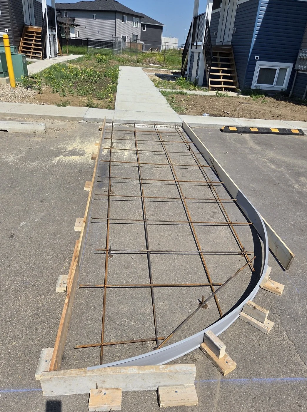 Foundation reinforcement for sidewalk or small structure with steel rebar laid in a grid on a concrete form, set in an asphalt parking lot, with wooden supports holding the form in place.