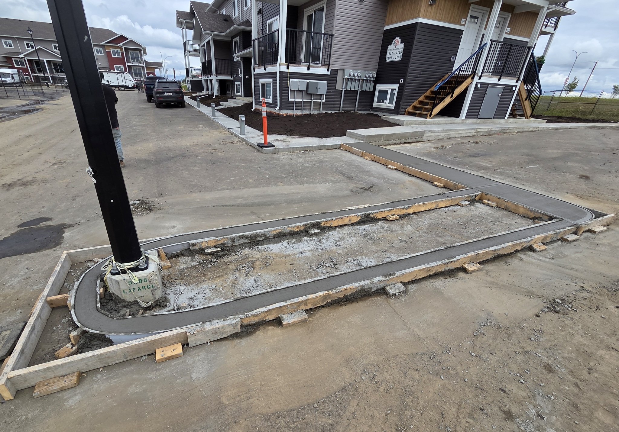 A close-up view of freshly poured commercial concrete radius curbs and custom wood formwork integrated around a parking lot light standard in Stony Plain near Spruce Grove.