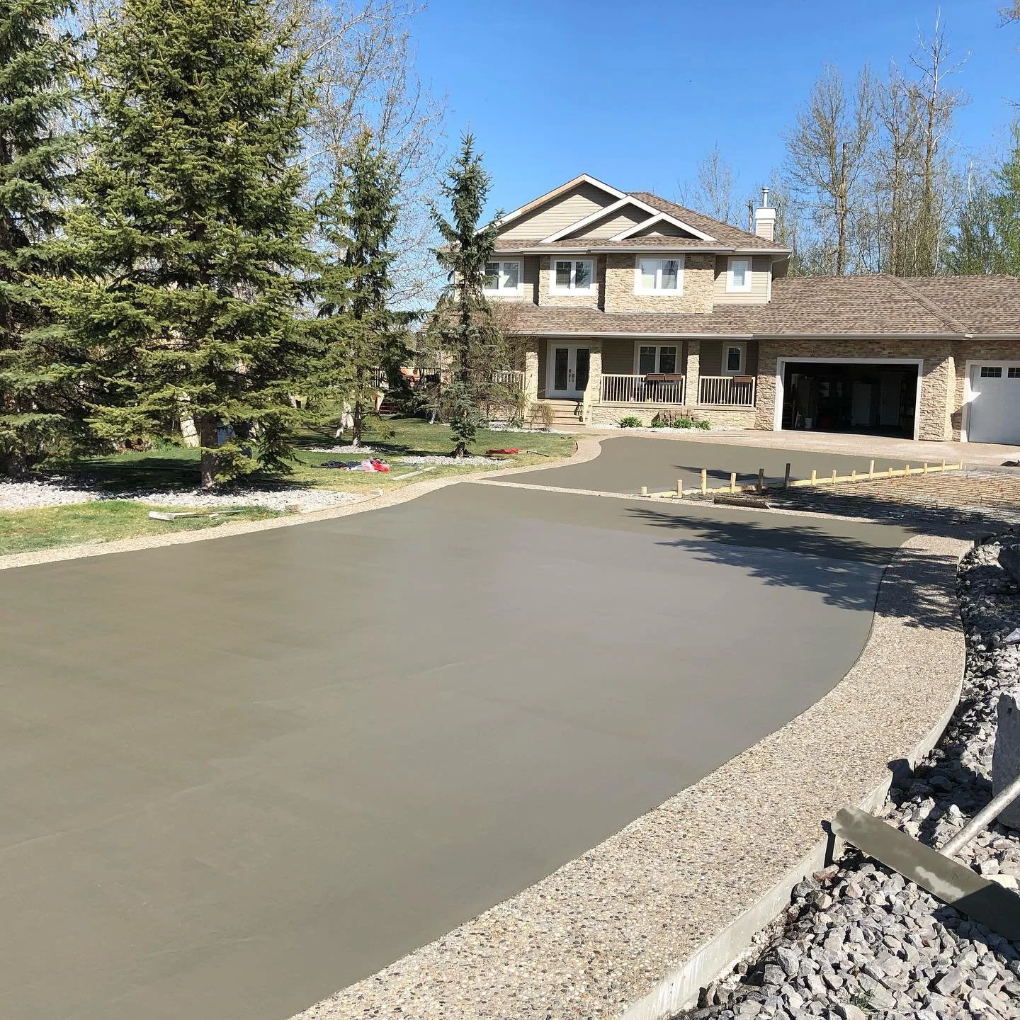 A large completed custom estate driveway featuring a smooth-finished main concrete slab paired with a clean exposed aggregate decorative border in the Greater Edmonton area.