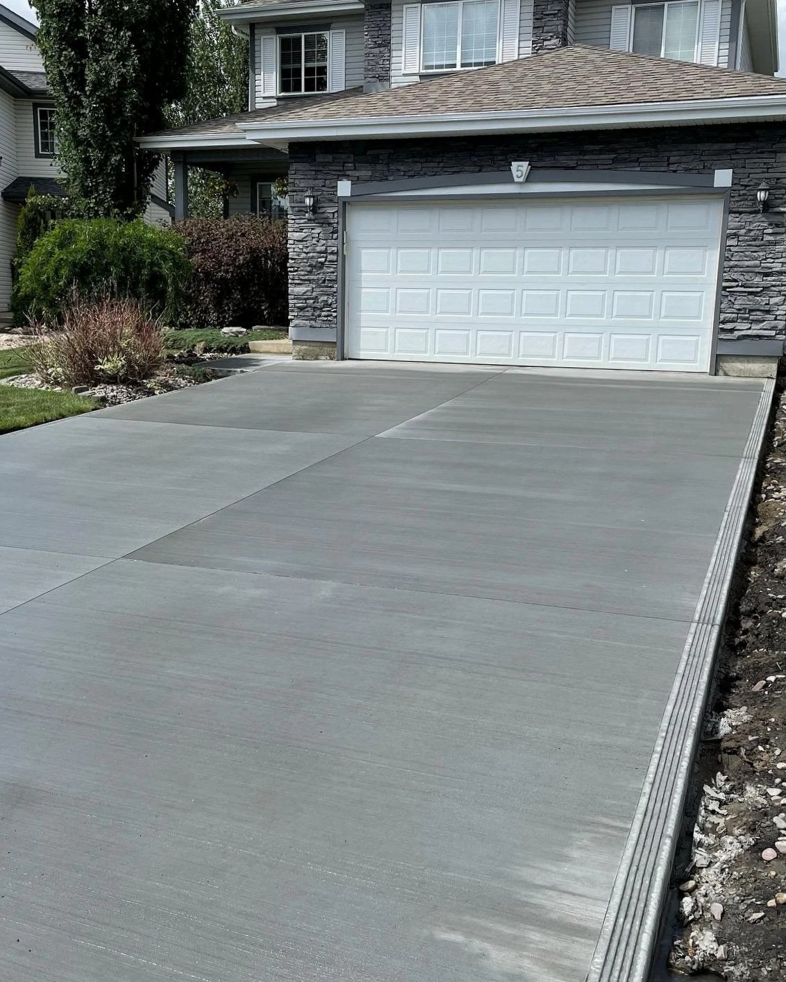 A freshly completed broom-finish concrete driveway featuring perfectly straight hand-tooled control joints and a clean picture-frame border layout in Stony Plain.