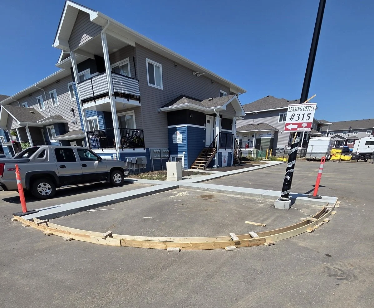 Construction of a new parking space in front of a multi-story apartment building, with wooden curbing and orange cones, and a sign indicating leasing office #315.