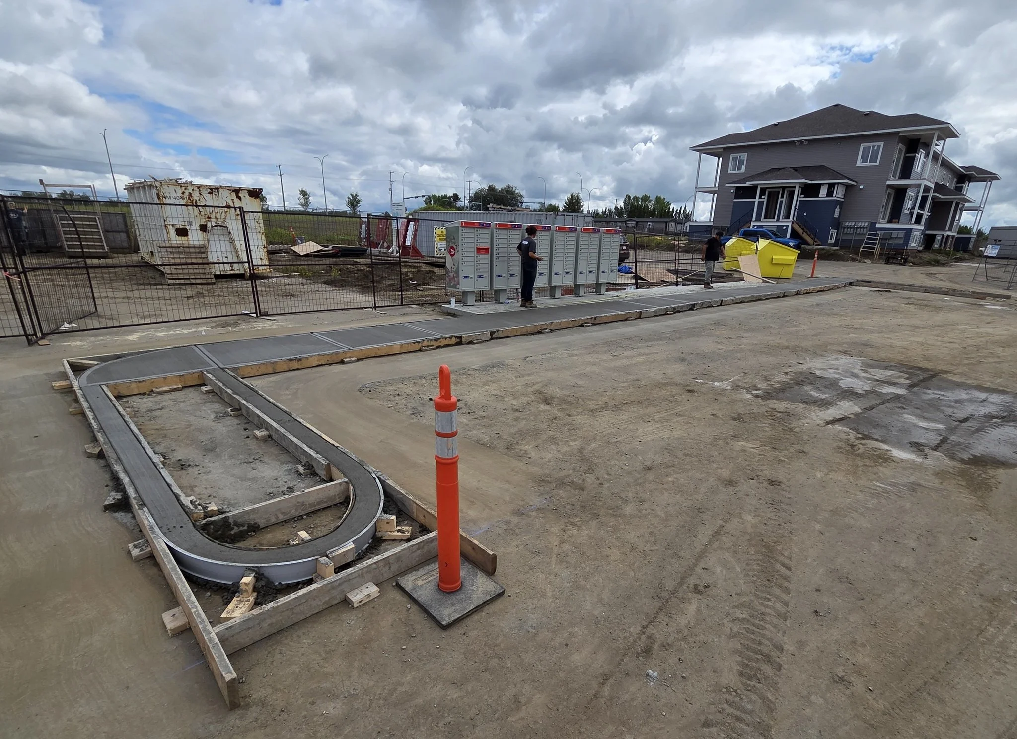 A professional concrete contractor crew finishing a commercial multi-family development sidewalk featuring precision radius curbs and a custom mail pad island in Stony Plain near Spruce Grove.