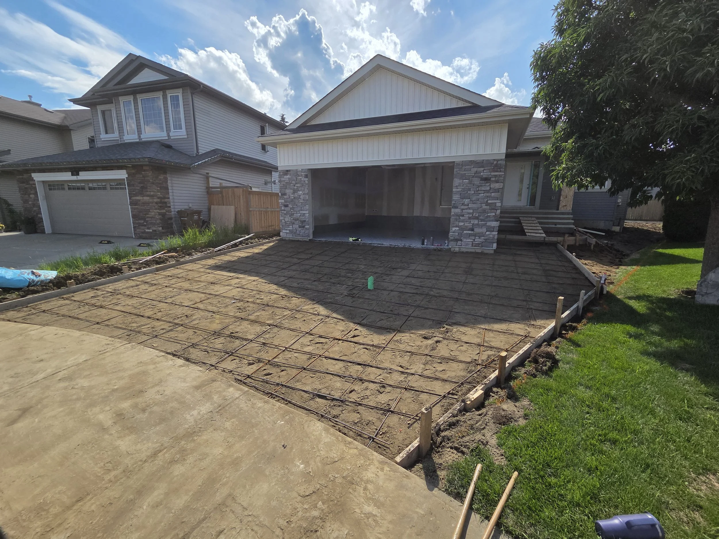Residential construction site prepped and ready with an unfinished concrete driveway, a house with some exterior siding, stone accents, and a garage. Ready for pour.