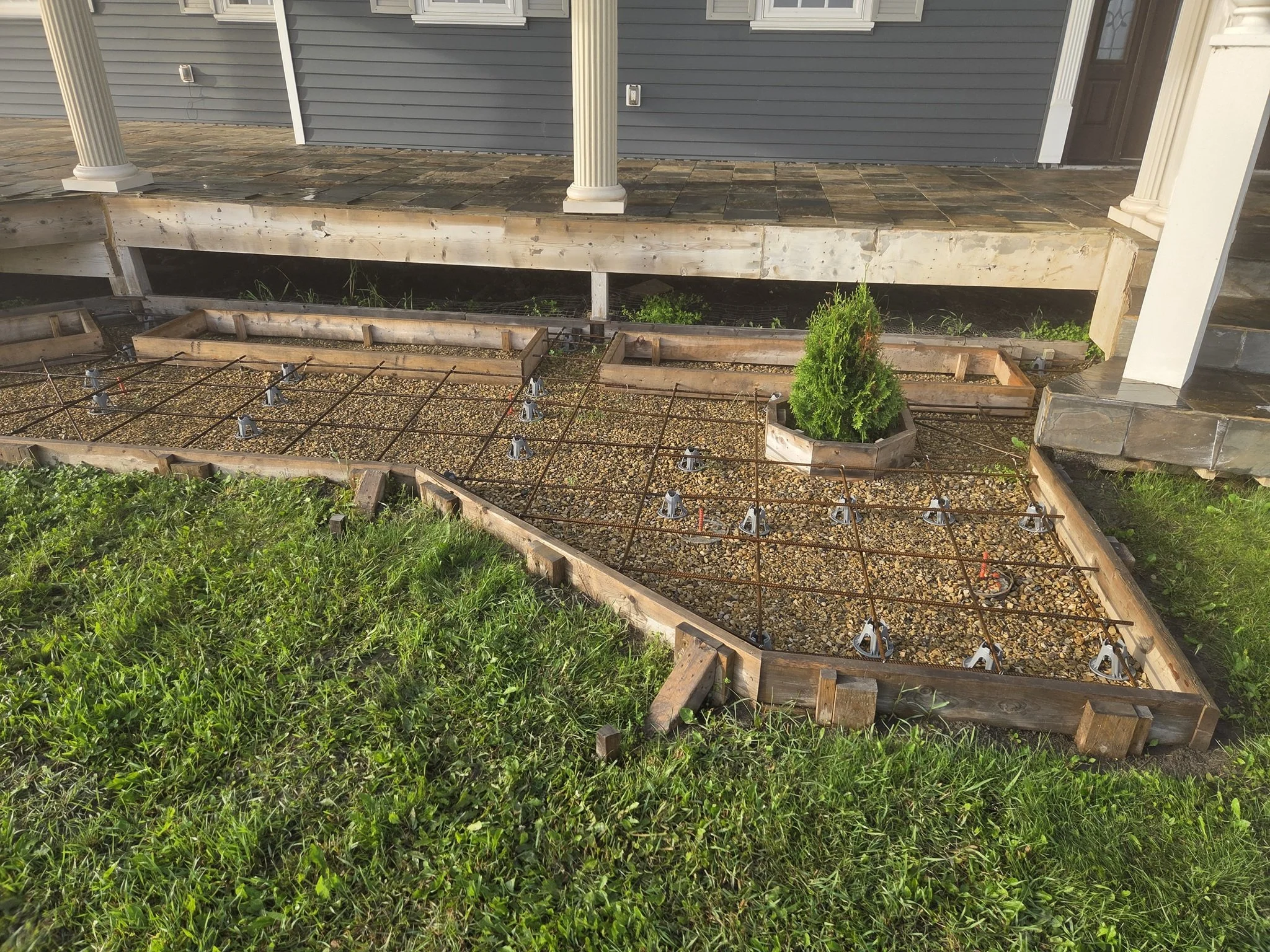 Detailed architectural concrete sidewalk formwork framing integrated garden beds and landscaping around a luxury country estate porch in Alberta.