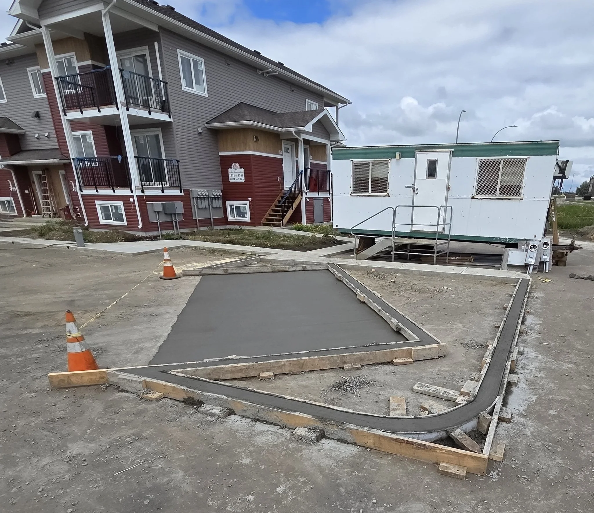 A freshly poured commercial concrete mail pad island featuring precision radius curves and wood formwork for a multi-family residential development in Stony Plain near Spruce Grove.