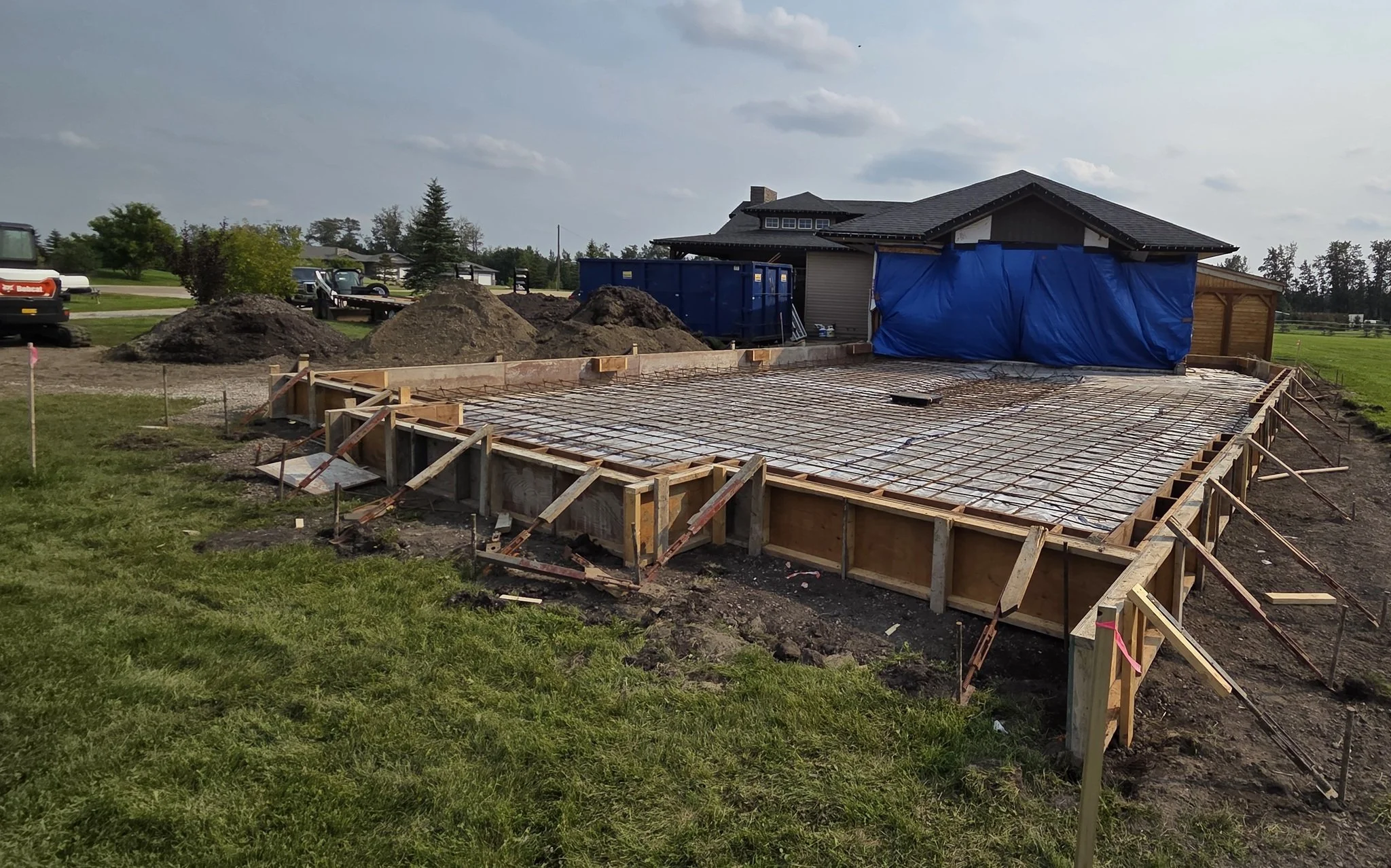 A side-profile view of massive residential concrete driveway formwork featuring robust heavy-duty wood bracing and on-site machinery on a Parkland County acreage near Spruce Grove.