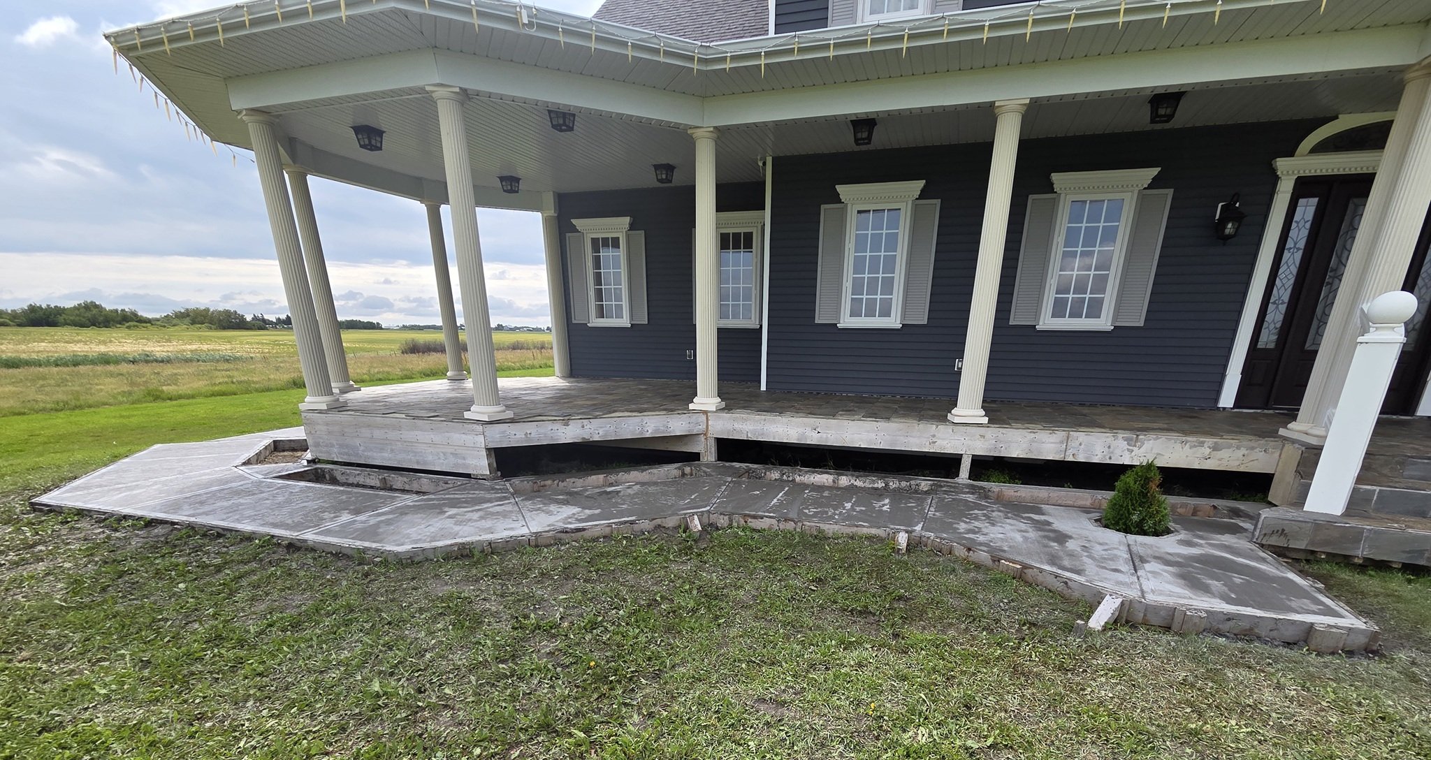 A completed large-scale architectural concrete walkway wrapping around a luxury country estate veranda on an Alberta acreage property.