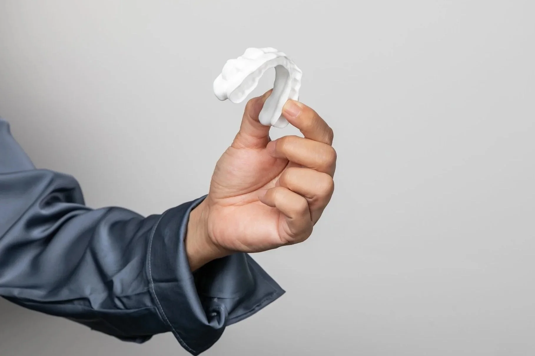 Person in a dark jacket holding a Mandibular Advancement Splint against a plain gray background.