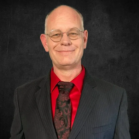 Richard in a black and red suite against a slate back drop